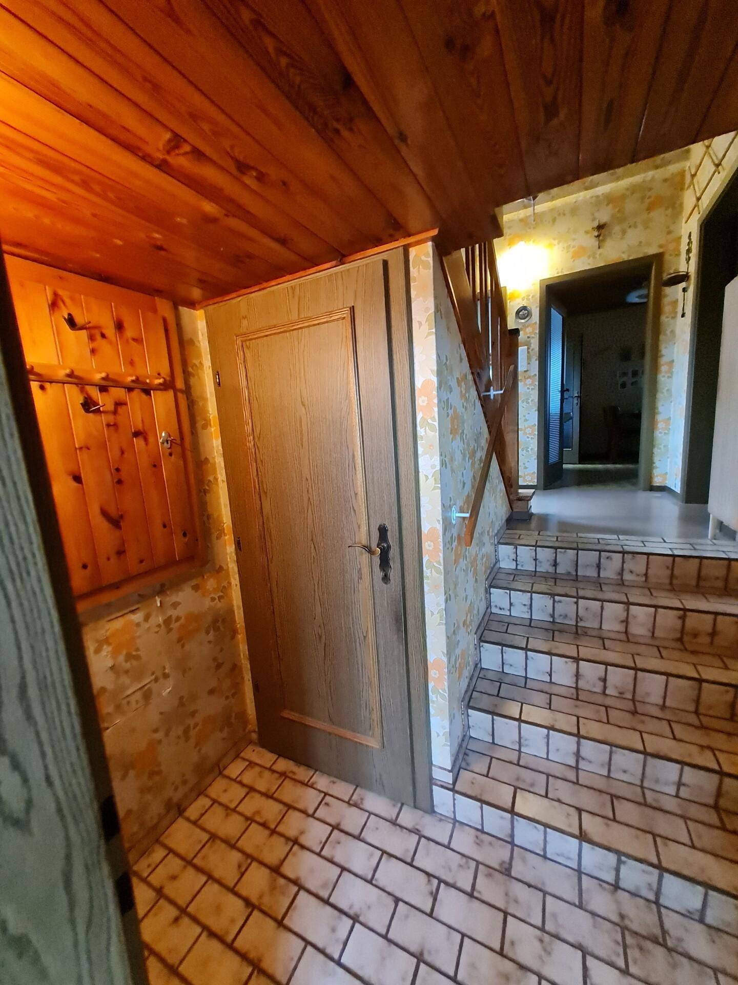 Eingangsbereich mit gefliestem Boden, Holzvertäfelung und Treppenaufgang.