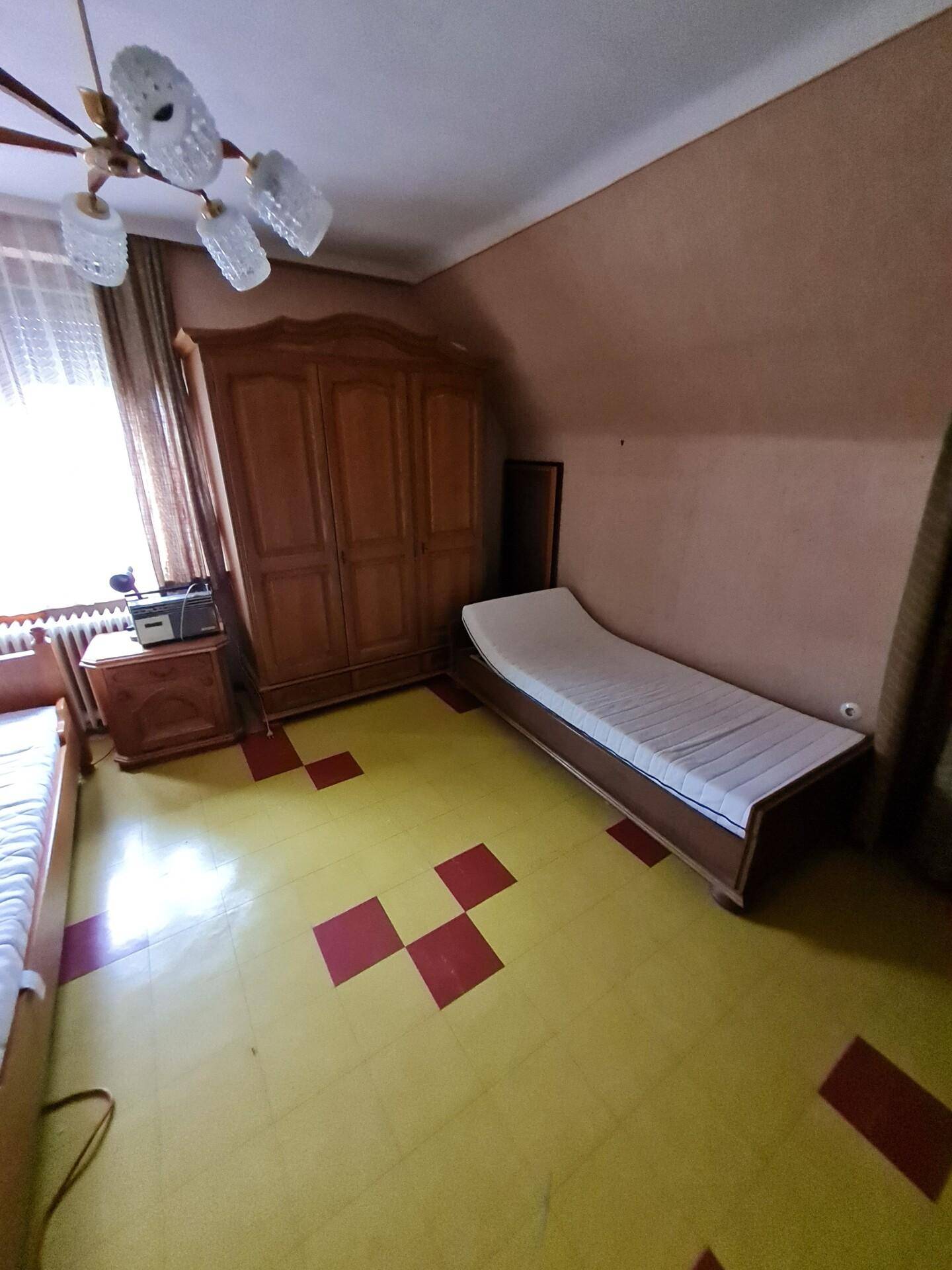 Schlafzimmer mit zwei Einzelbetten, Schrank und gemustertem Boden.