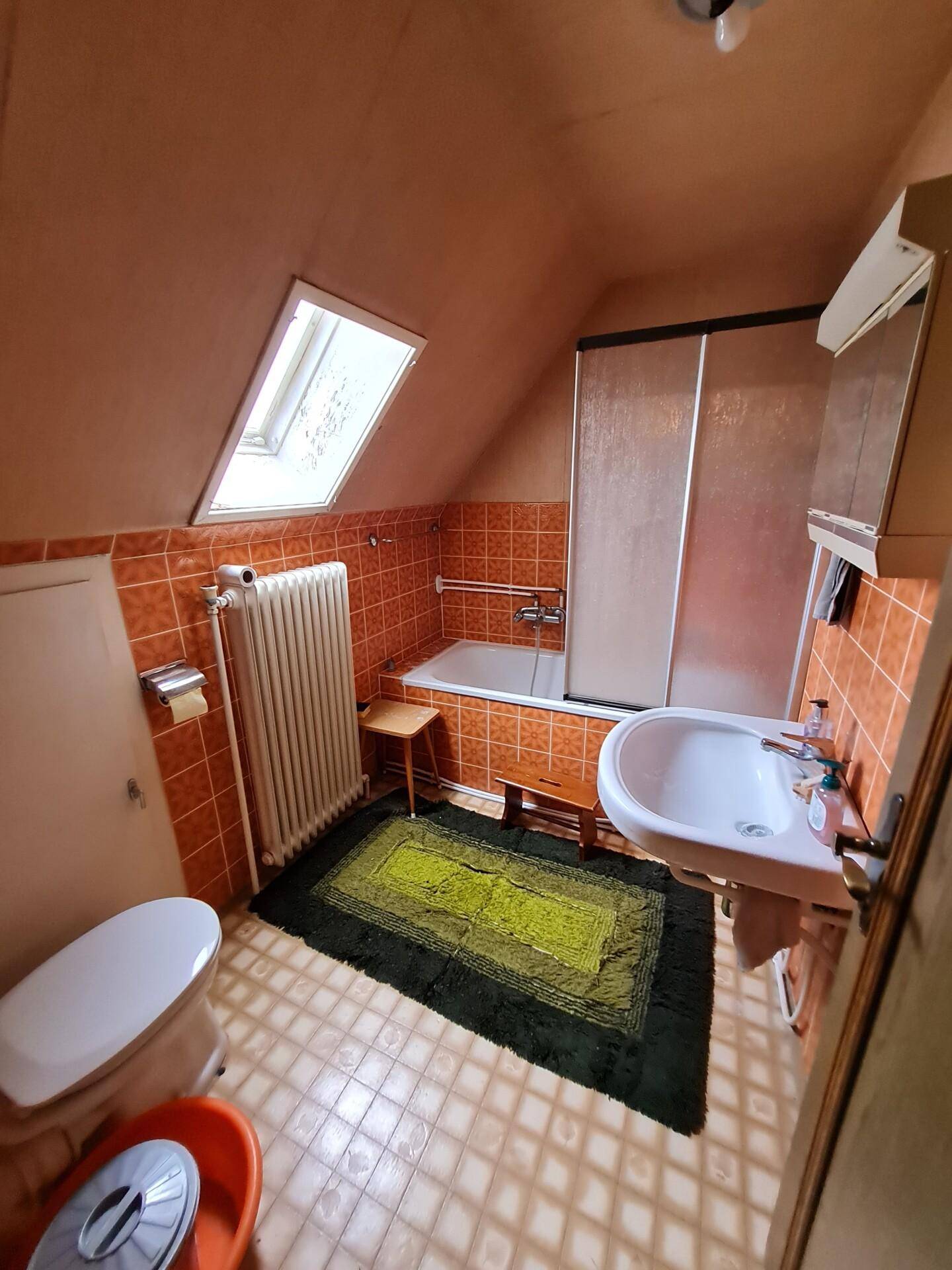 Badezimmer mit Badewanne, Waschbecken, WC und Dachfenster, in orangefarbenen Fliesen.