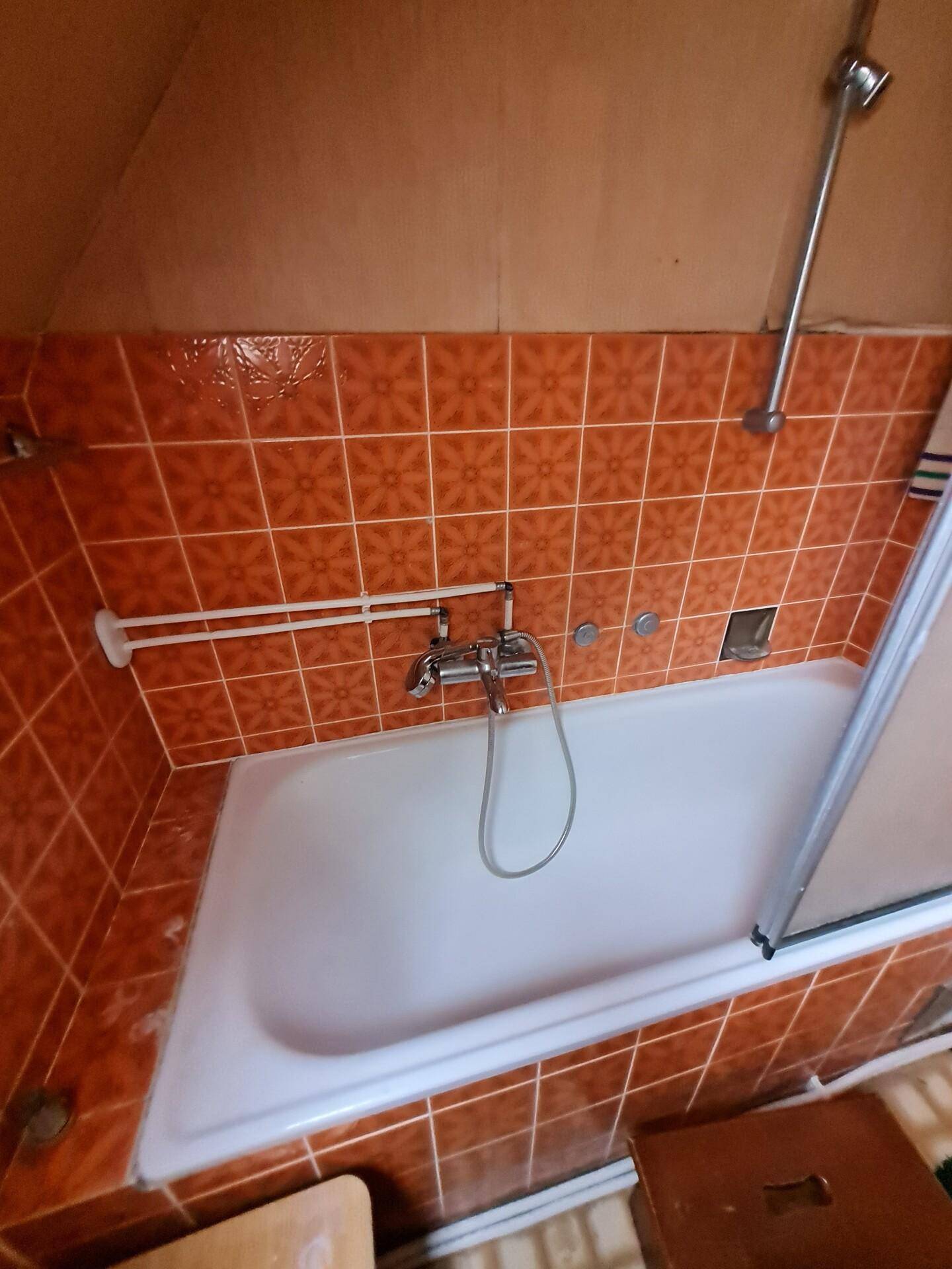 Badewanne mit Duschabtrennung und orangefarbenen Wandfliesen in einem traditionellen Badezimmer.