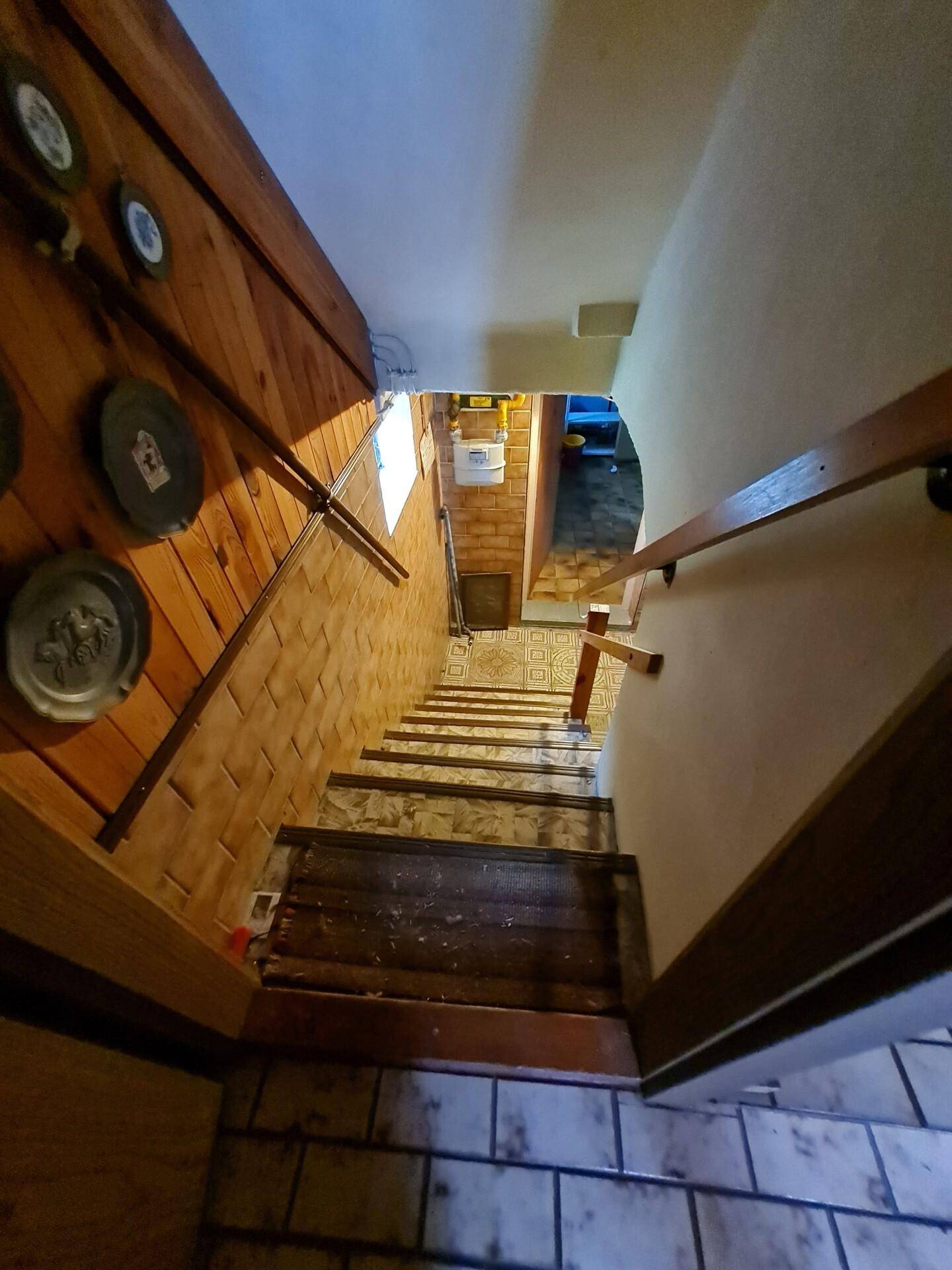 Treppenabgang in den Keller mit gefliestem Boden und Holzvertäfelung.