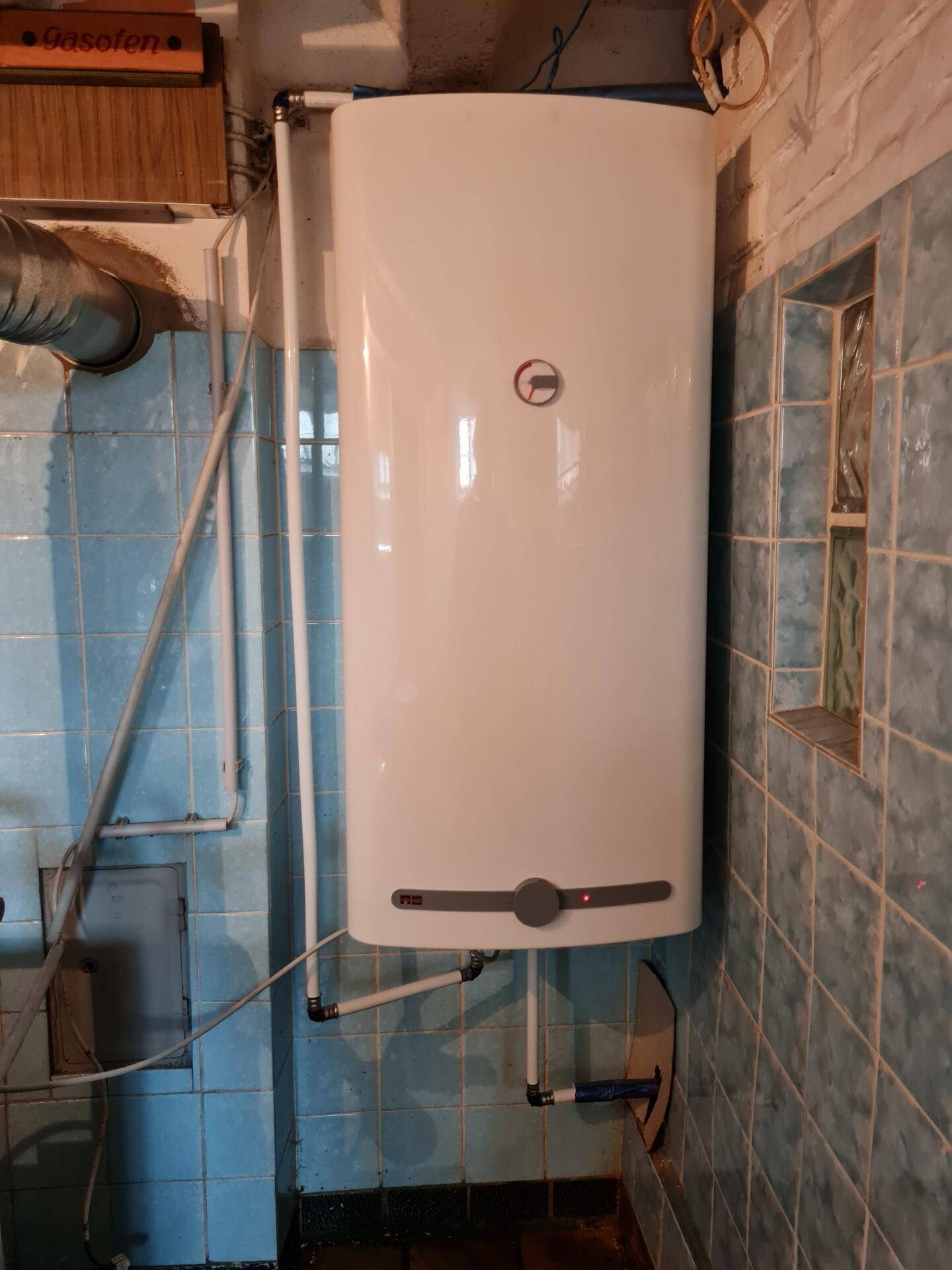 Warmwasserbereiter an der Wand in einem gefliesten Kellerraum.