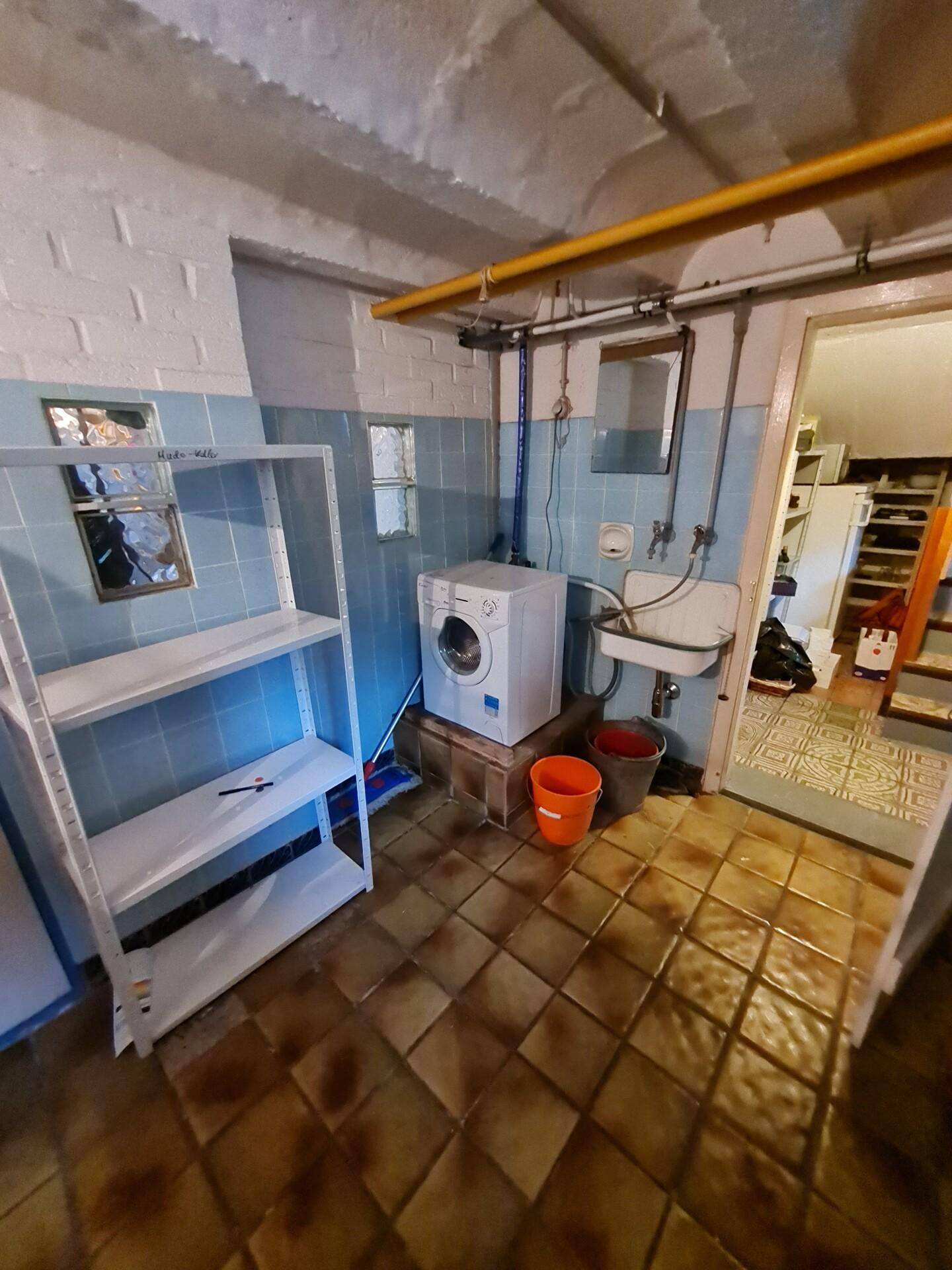 Waschküche im Keller mit Waschmaschine, Regalen und Waschbecken.