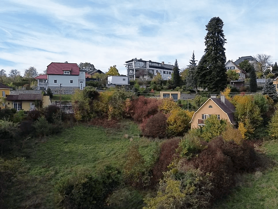Luftaufnahme einer Wohnsiedlung am Hang mit verschiedenen Häusern und üppiger Vegetation in Herbstfarben.