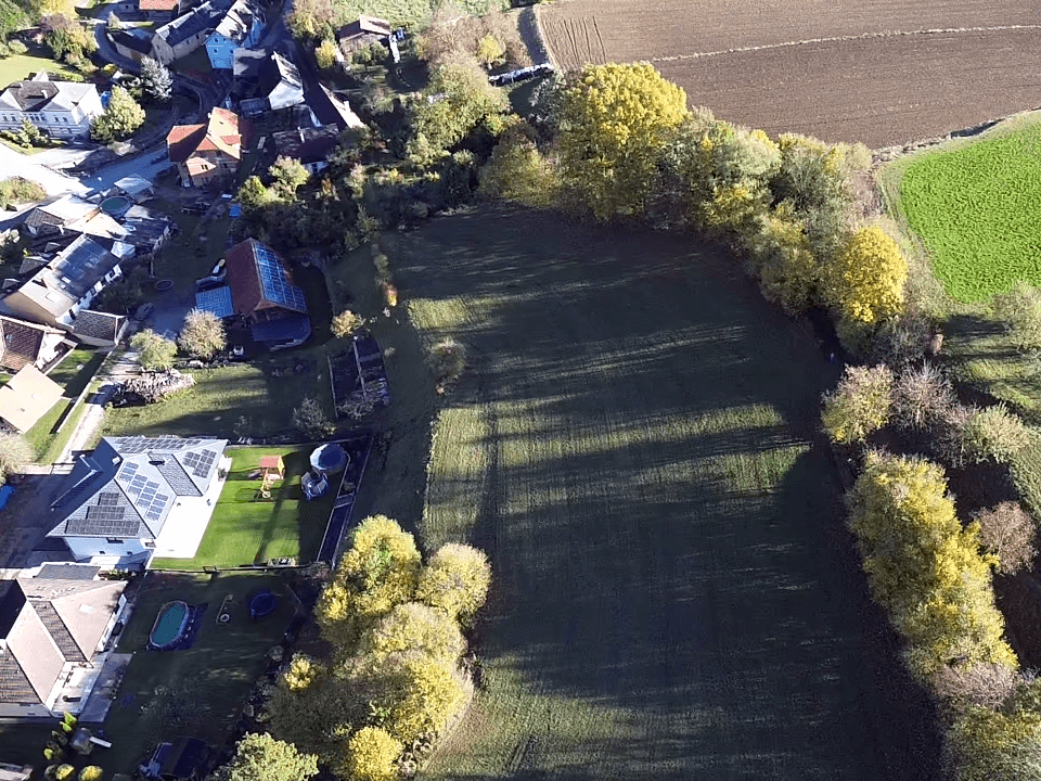 Luftaufnahme einer großen Wiese neben Wohnhäusern mit Gärten und Solaranlagen, angrenzend an Felder.