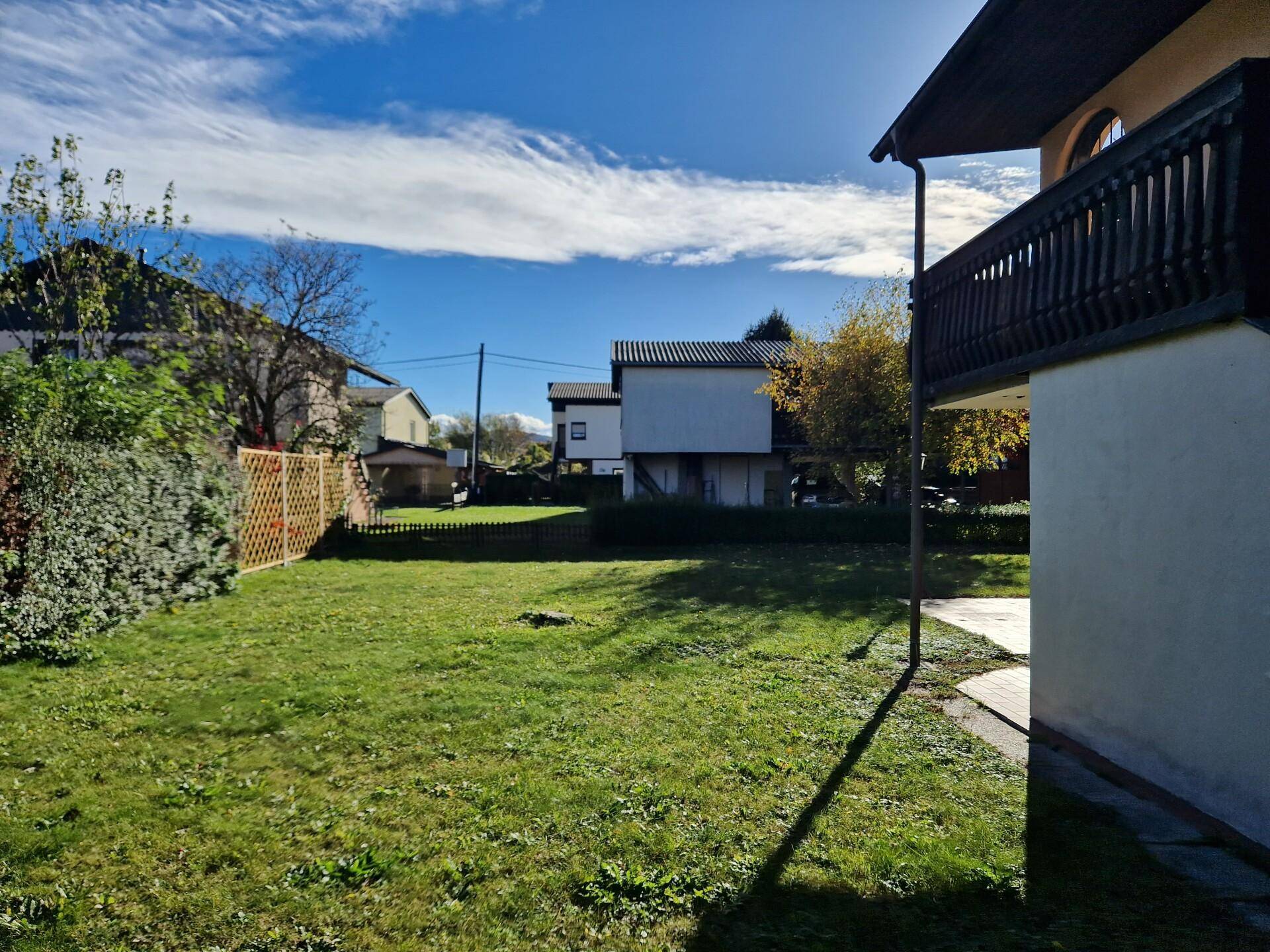 Seitlicher Gartenbereich mit Rasenfläche und Blick auf die Nachbarschaft unter blauem Himmel.