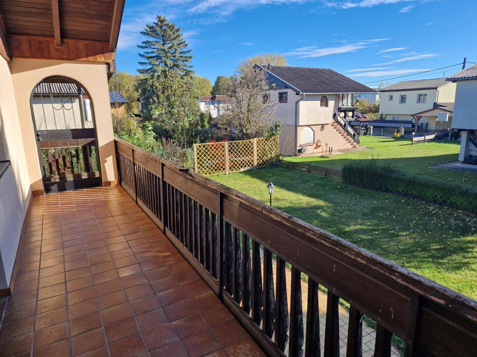 Geräumiger Balkon mit Holzgeländer und Fliesenboden, bietet Blick auf den Garten und die Umgebung.