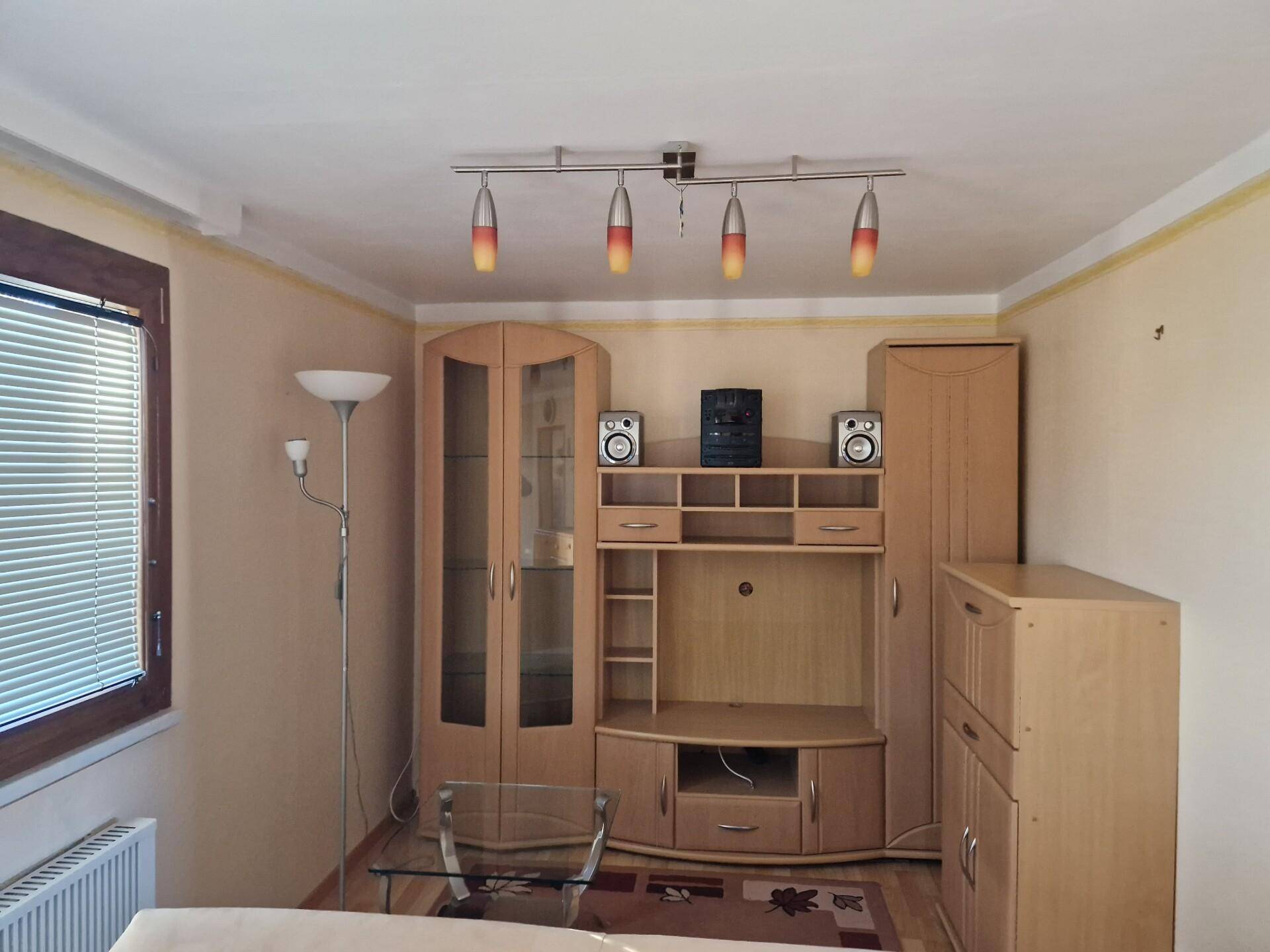 Gemütliches Wohnzimmer mit Holzmöbeln, Parkettboden und Fenster mit Jalousien.