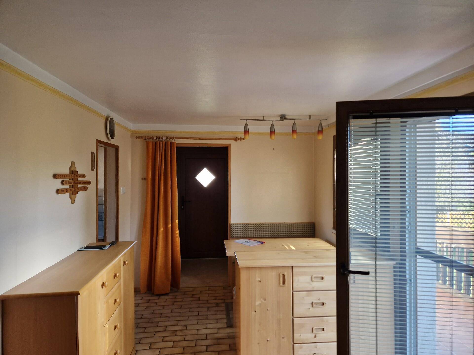 Heller Eingangsbereich mit Holzmöbeln, Fliesenboden und Zugang zum Balkon.