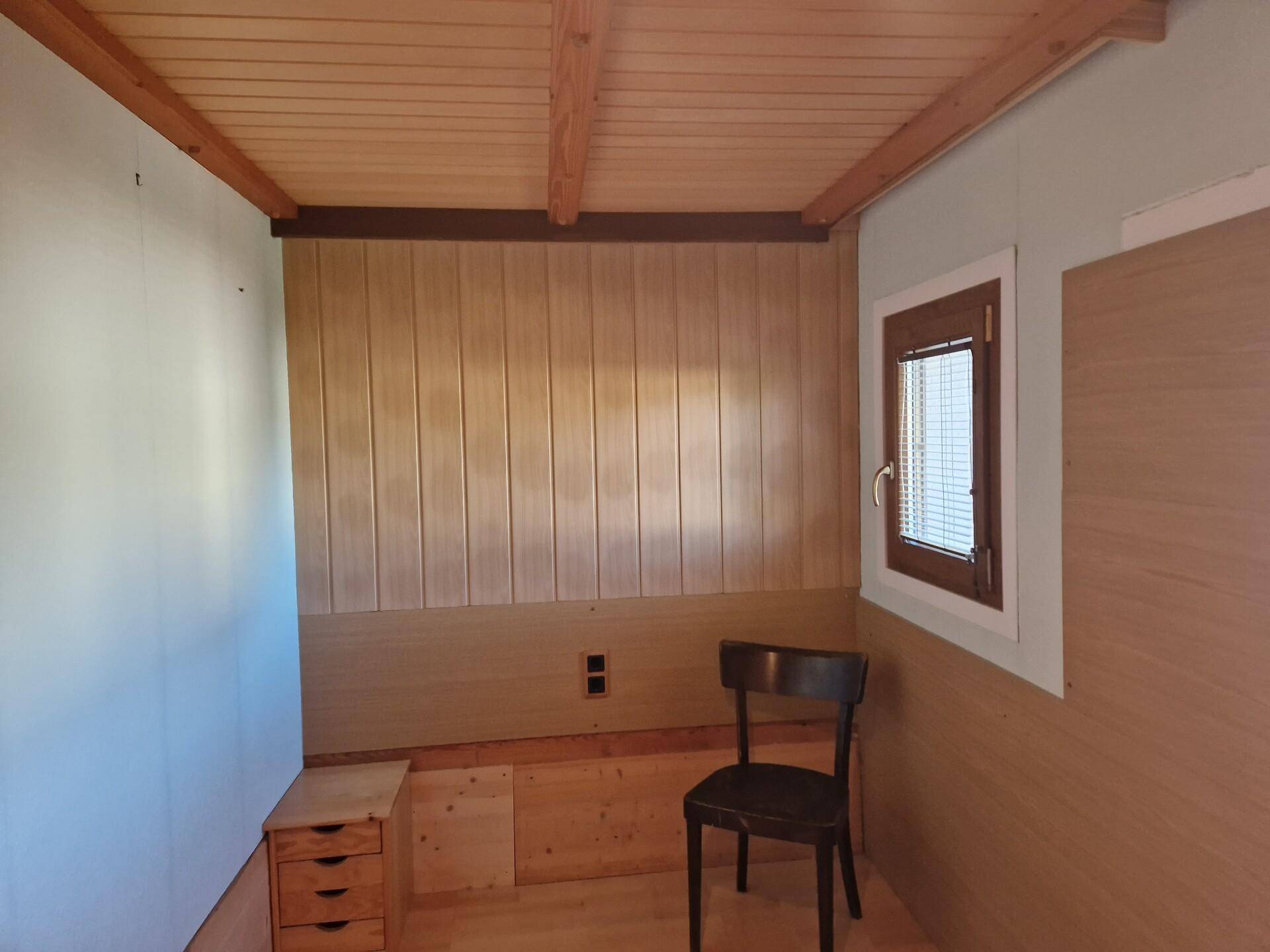 Kleines Schlafzimmer mit Holzvertäfelung, Holzbalkendecke und Fenster für natürliches Licht.
