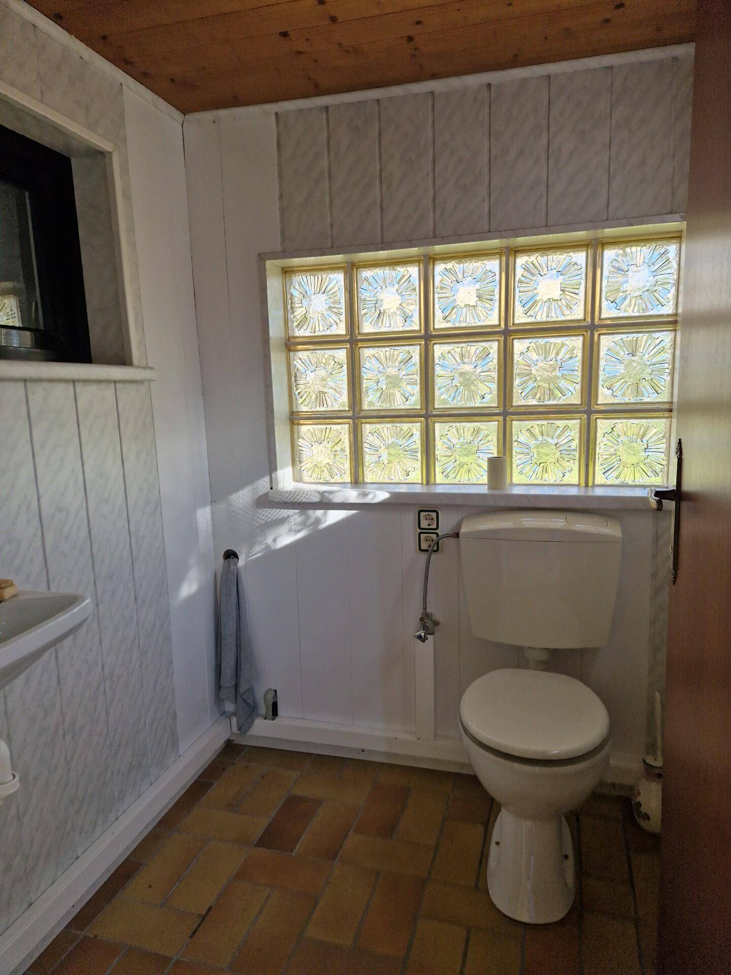 Helles WC mit Fliesenboden, Toilette und Fenster aus Glasbausteinen für Privatsphäre.