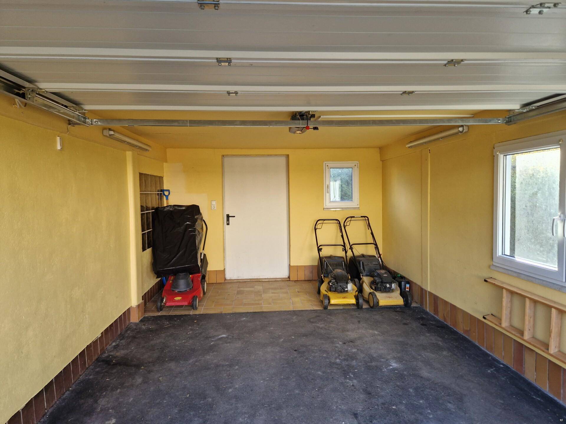 Geräumige Garage mit gelben Wänden, Betonboden und Fenstern für Belüftung.