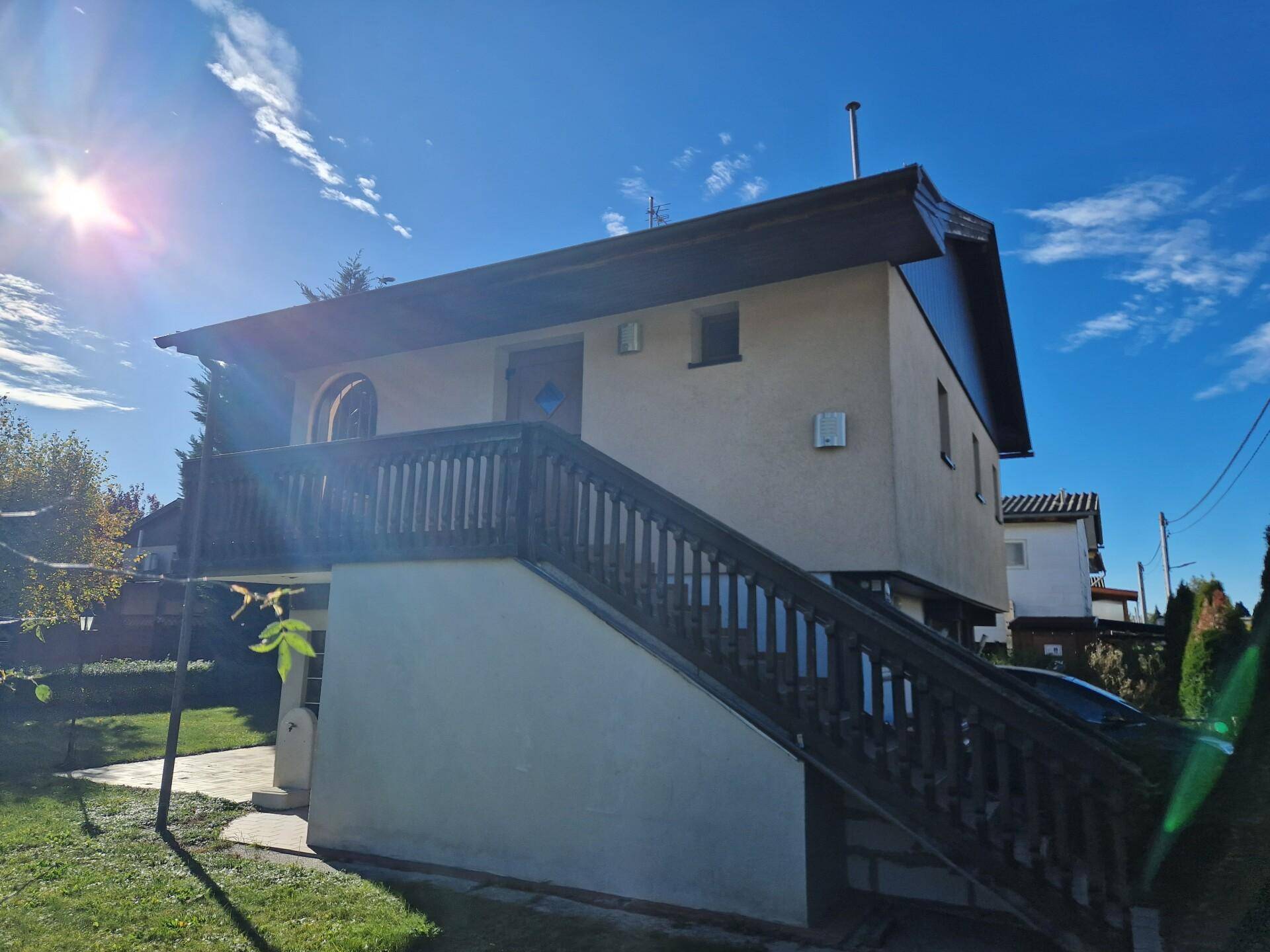 Seitenansicht des Hauses mit Außentreppe zum Balkon und sonnigem Gartenbereich.