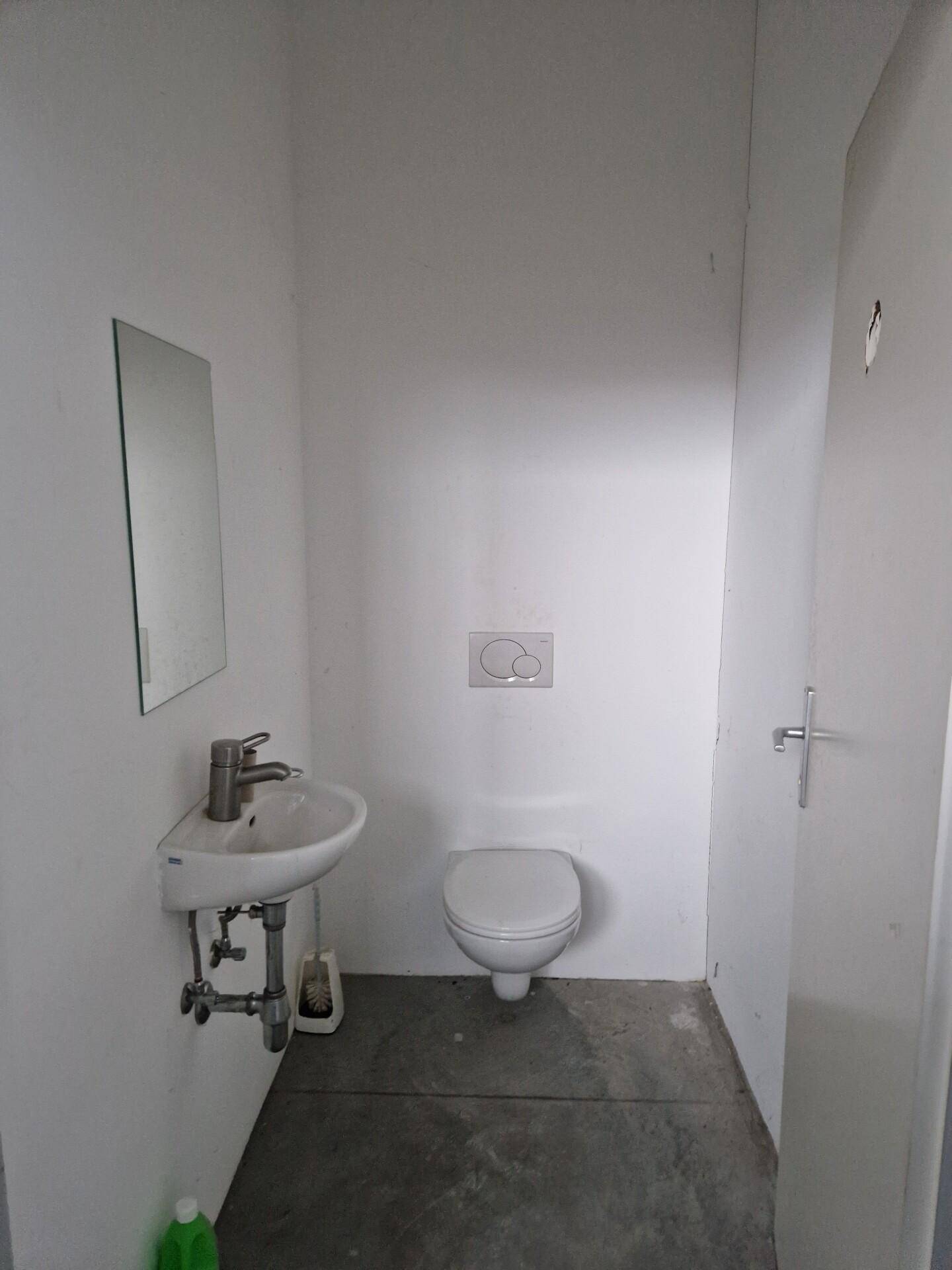 Einfache Gästetoilette mit wandhängendem WC, kleinem Waschbecken und Spiegel.