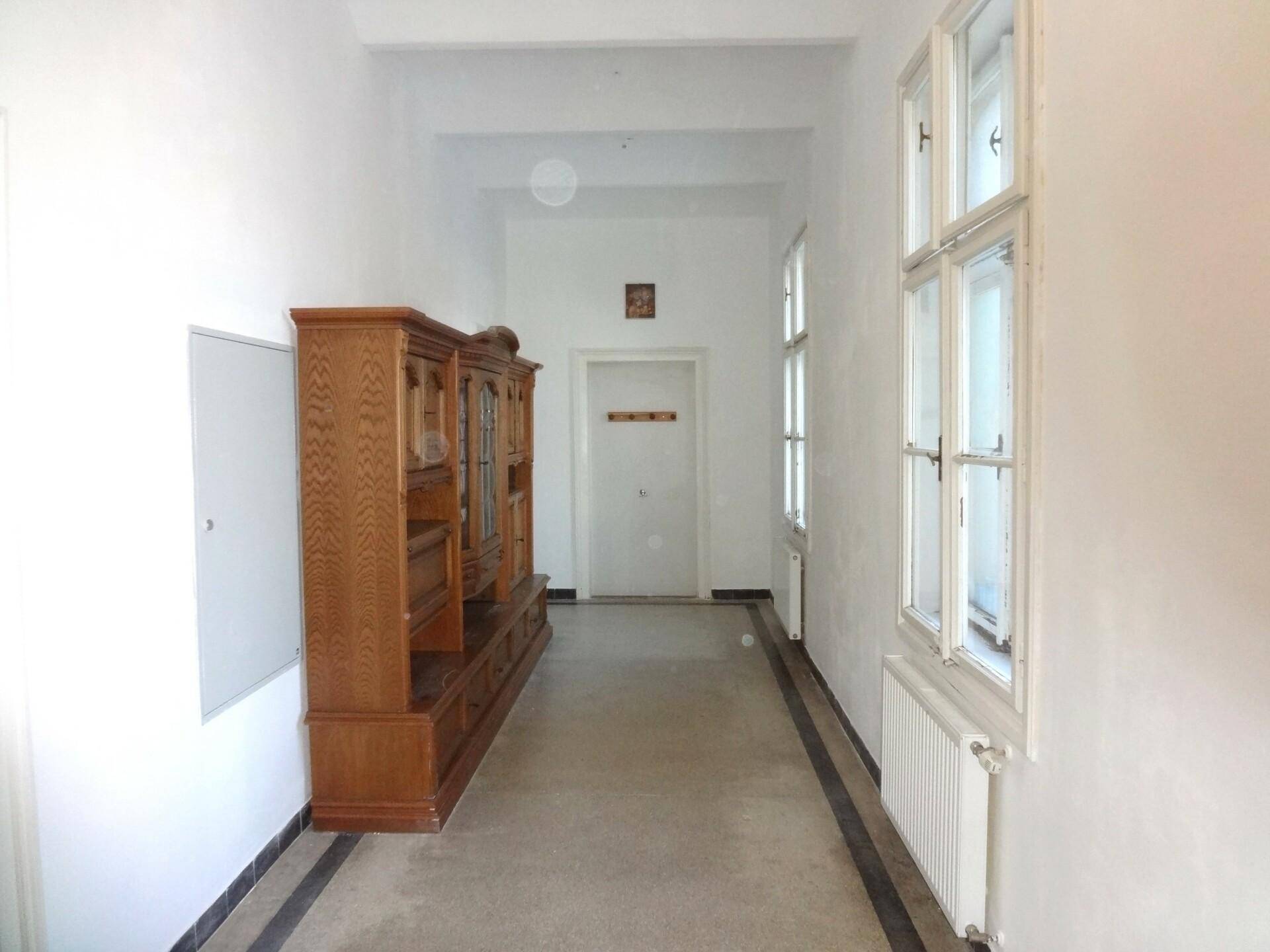 Langer Flur mit einem großen Holzschrank, mehreren Fenstern und einem Teppichläufer auf Fliesenboden.