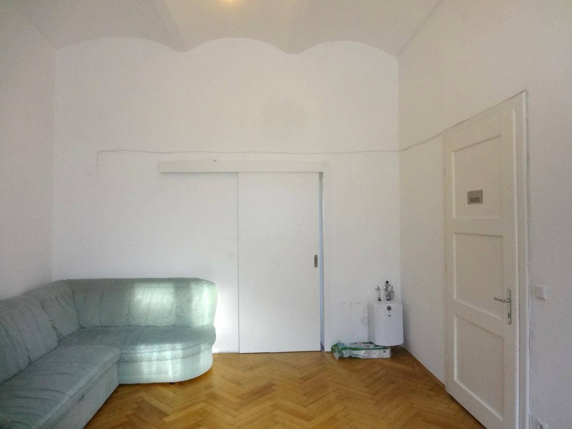Wohnzimmer mit einem Sofa, einer Schiebetür und einer weiteren Tür, ausgestattet mit Fischgrätparkett.