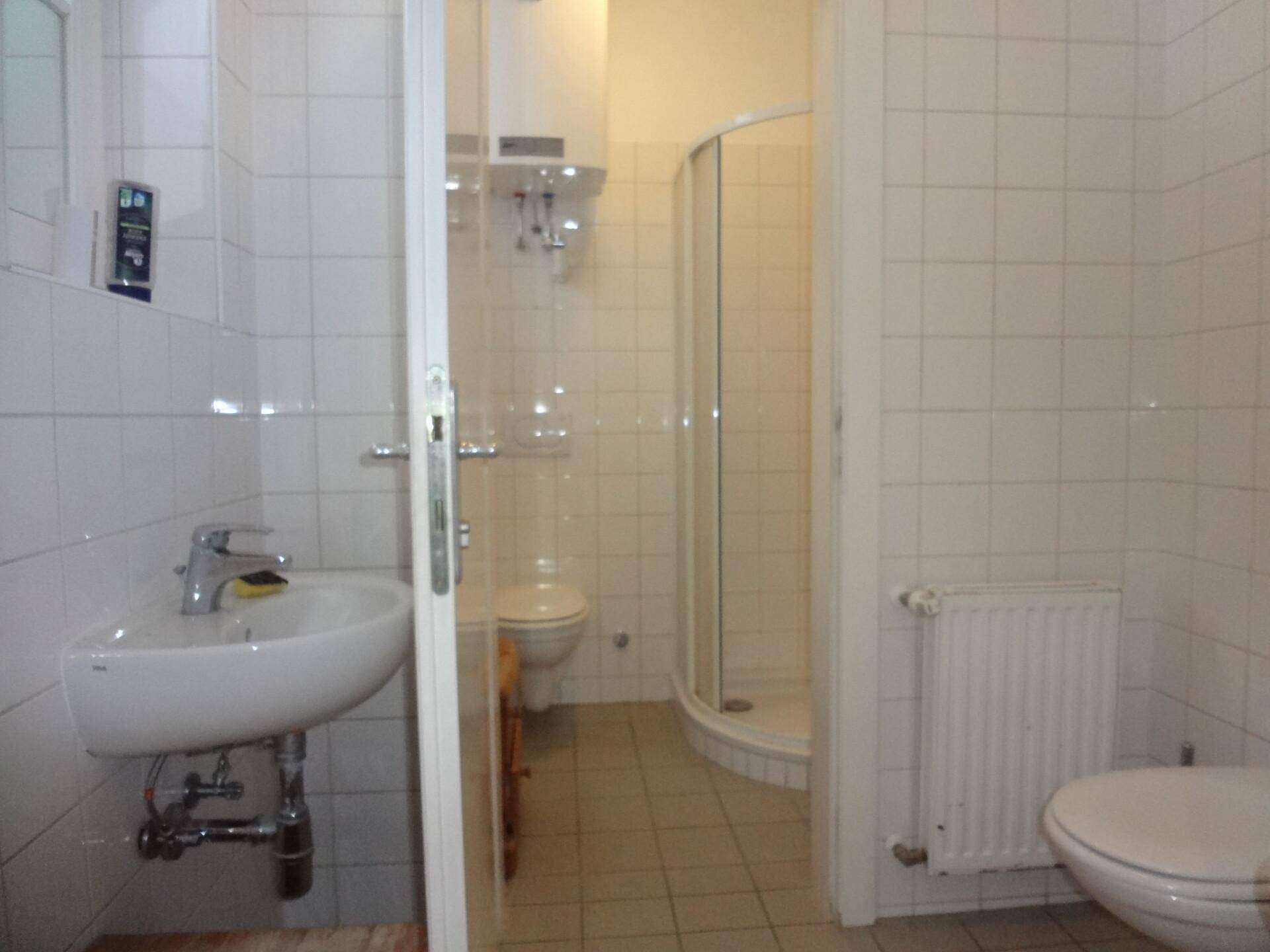 Badezimmer mit Duschkabine, Waschbecken und Toilette, komplett gefliest in Weiß.