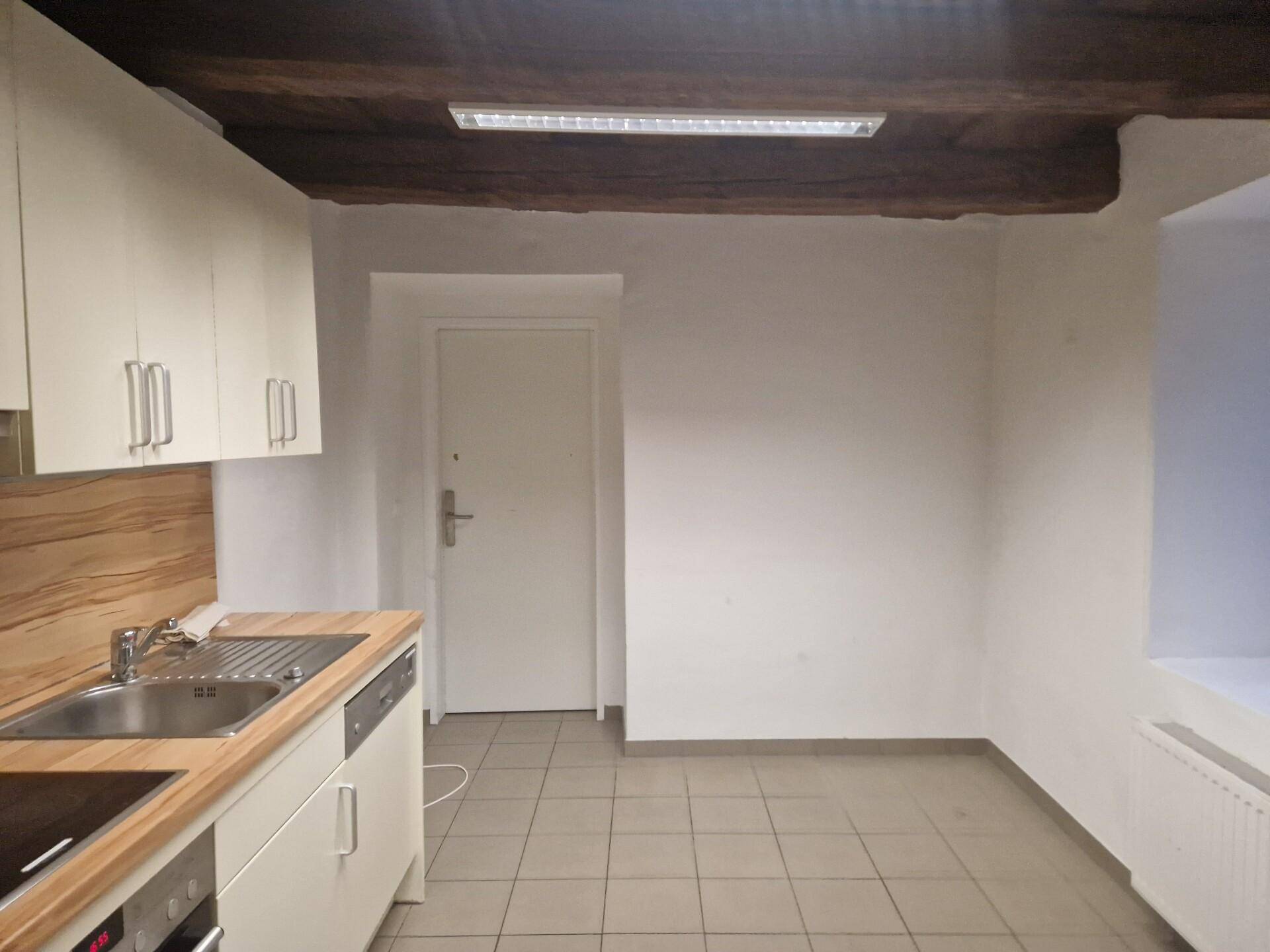 Kleine Küche mit hellen Schränken, Holztheke und sichtbaren Deckenbalken, gefliester Boden.