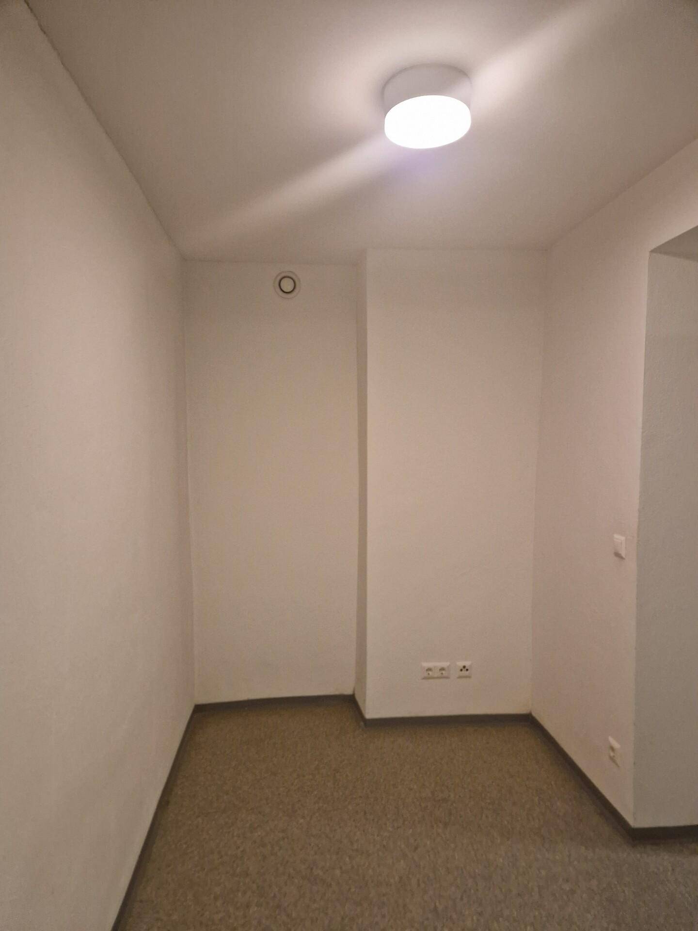 Leerer Raum mit weiß gestrichenen Wänden und Linoleumboden, ohne Fenster, mit Deckenleuchte.