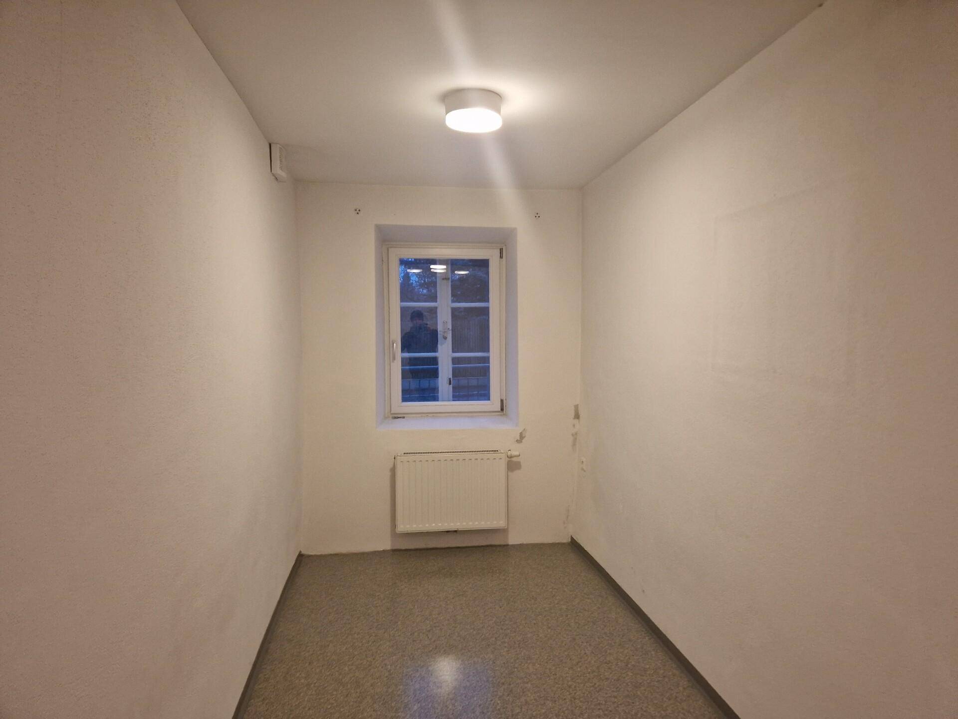Kleiner, heller Raum mit einem Fenster, Heizkörper und Linoleumboden, geeignet als Einzelbüro.