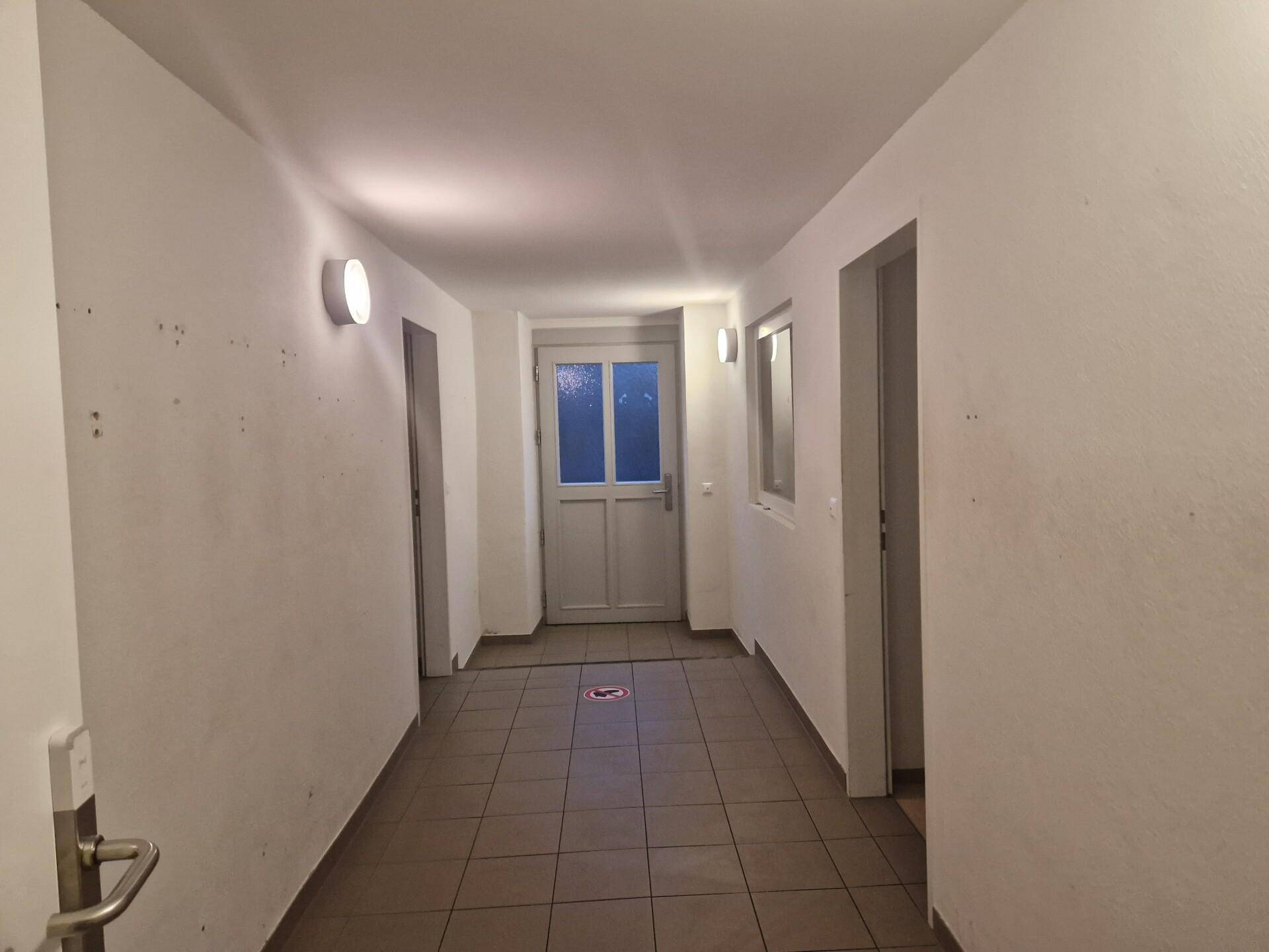 Langer Flur mit gefliestem Boden, weiß gestrichenen Wänden und mehreren Türen, gut beleuchtet.