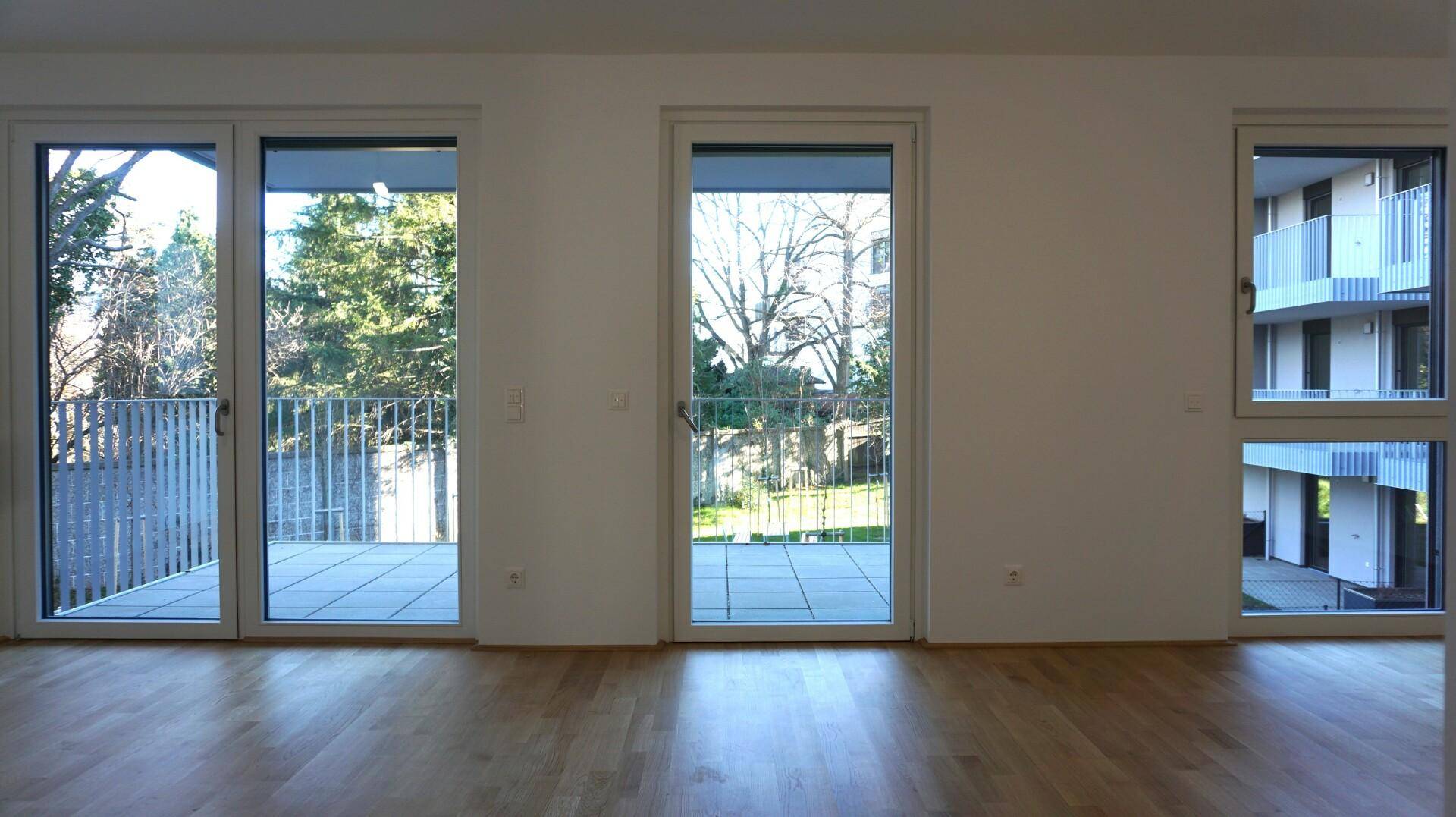Geräumiges Zimmer mit Parkettboden und Zugang zu einem Balkon, der einen Blick ins Grüne bietet.