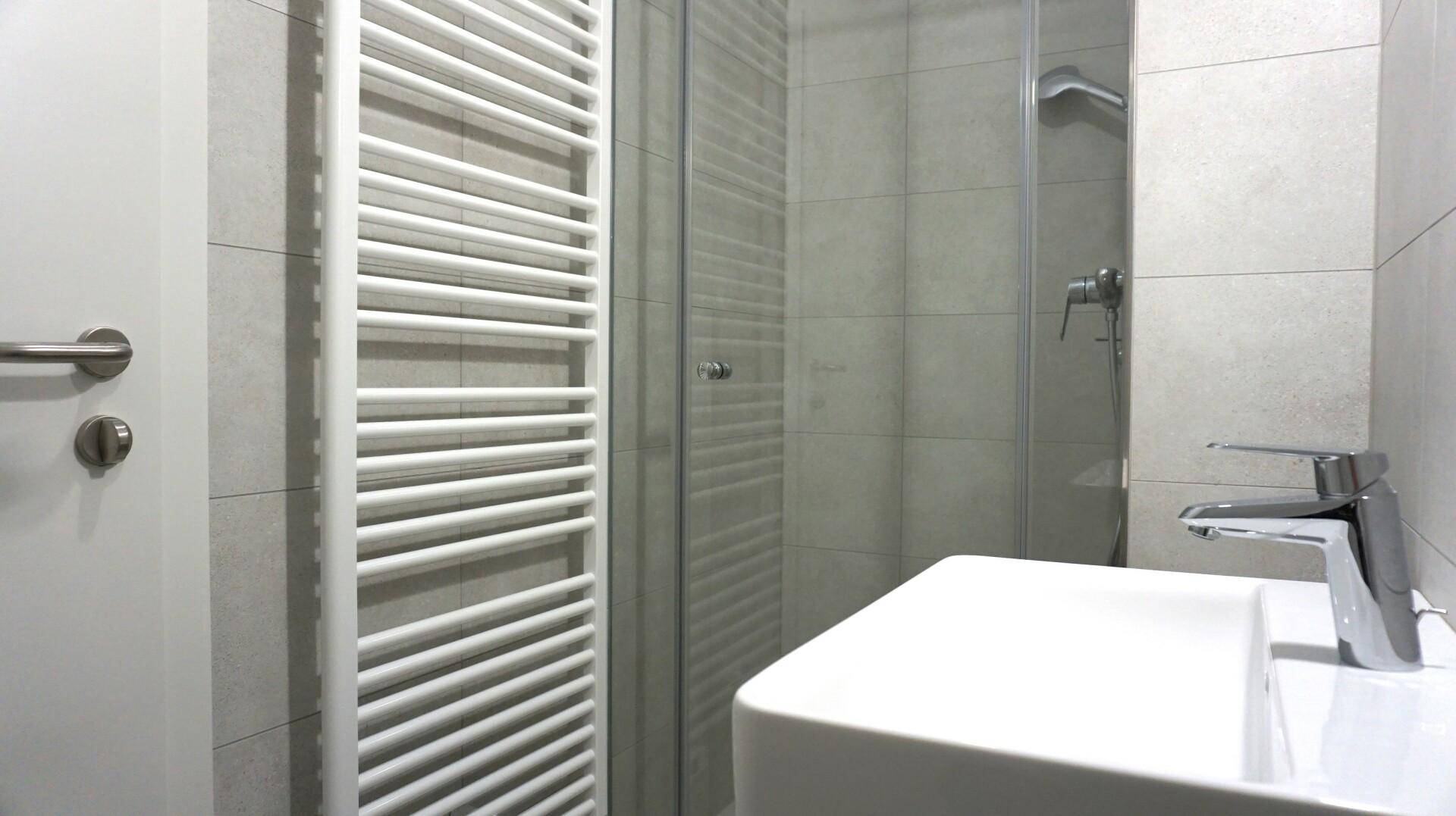 Modernes Badezimmer mit grauen Fliesen, Duschkabine und einem beheizten Handtuchhalter.