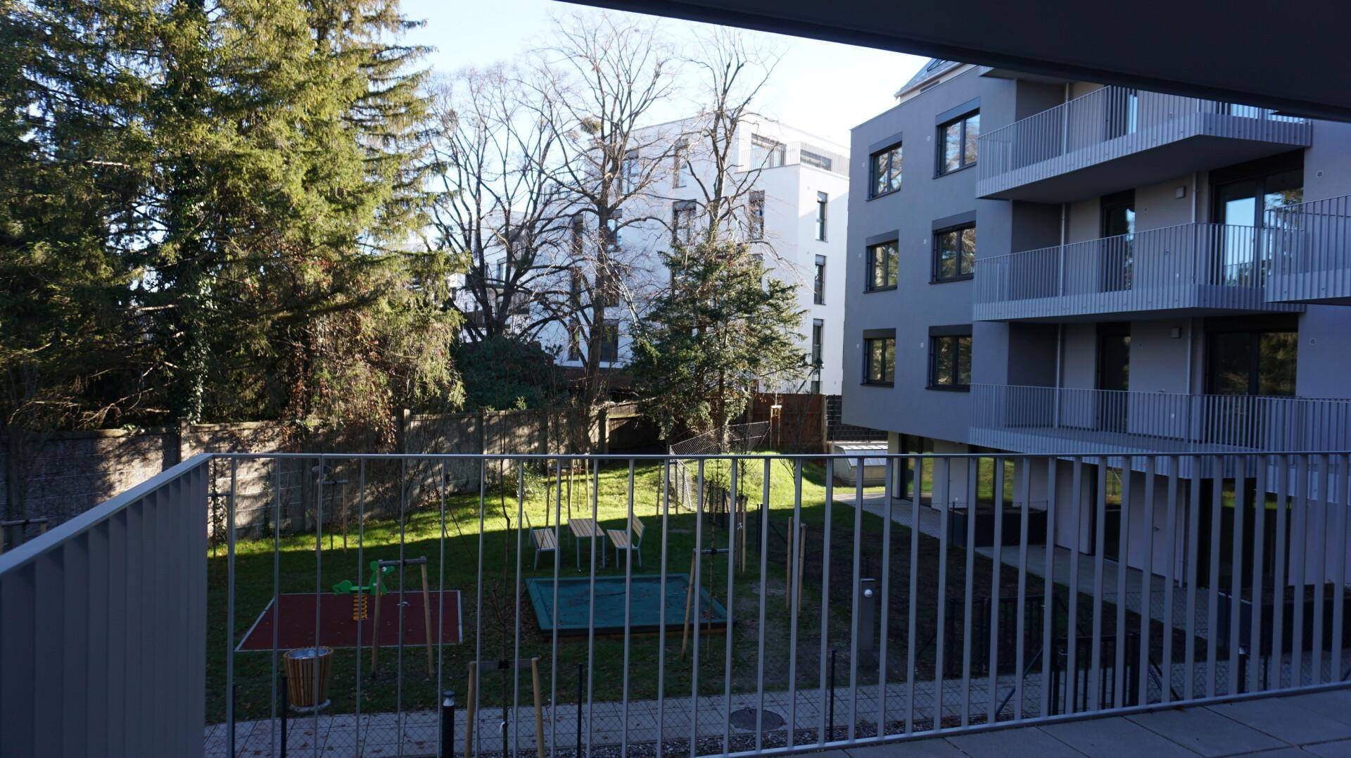Blick vom Balkon auf den Gemeinschaftsgarten mit Spielplatz und umliegenden Gebäuden.