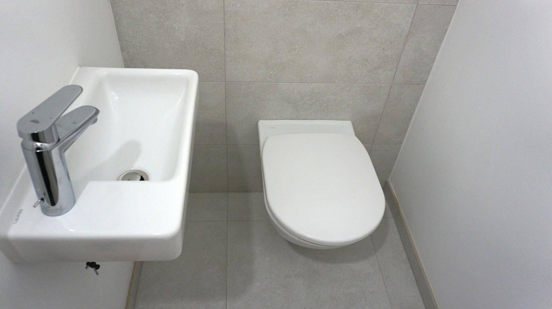 Modernes Gäste-WC mit wandhängender Toilette, kleinem Waschbecken und hellen Fliesen.