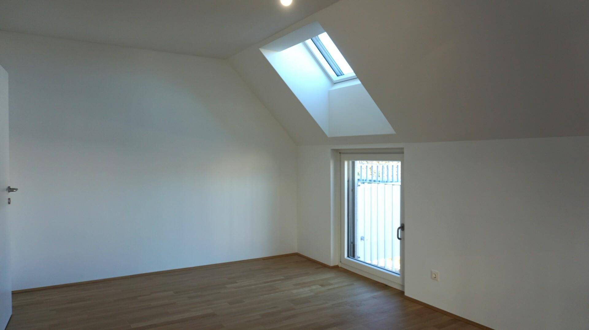 Lichtdurchfluteter Dachgeschossraum mit Dachfenster und Zugang zu einem Außenbereich.