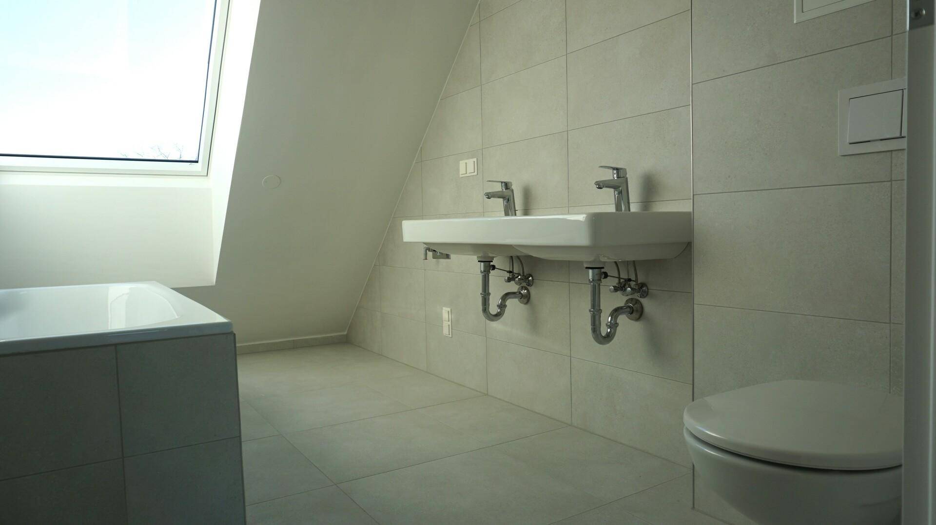 Helles Badezimmer im Dachgeschoss mit Doppelwaschbecken, Badewanne und Dachfenster.