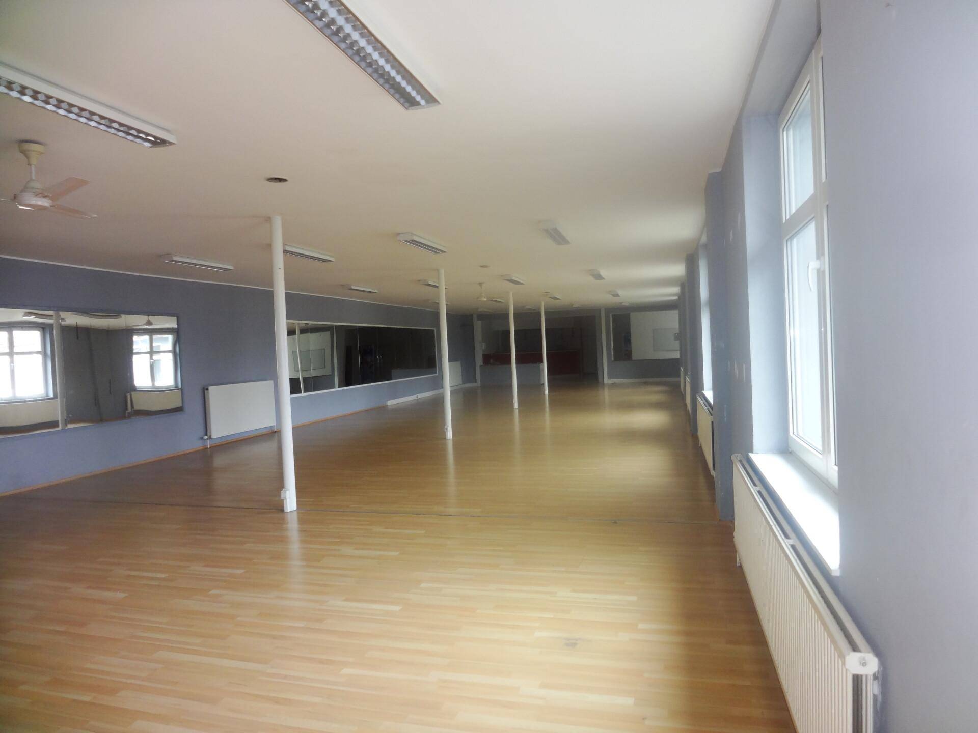 Großer, heller Raum mit Holzfußboden, Spiegelwänden und Deckenventilatoren, ideal für Fitness oder Tanz.