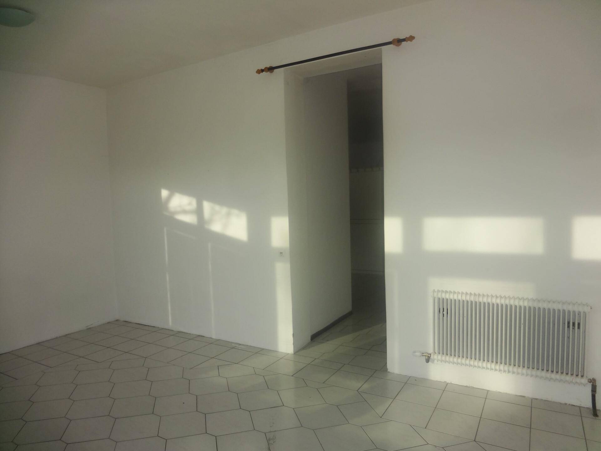 Leerer Raum mit Fliesenboden, weiß gestrichenen Wänden und Heizkörper, durch Sonnenlicht erhellt.