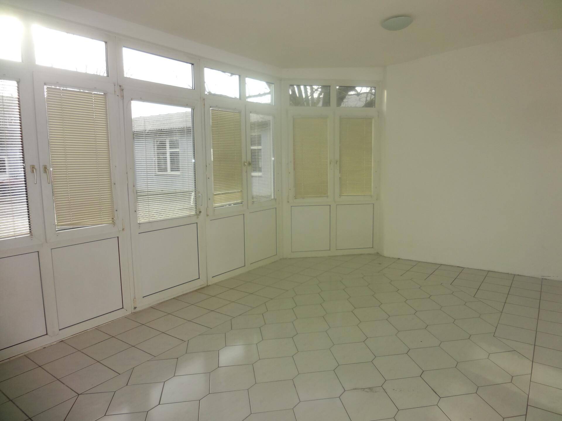 Heller Raum mit vielen Fenstern und Türen, Fliesenboden und Jalousien, ideal als Wintergarten oder Anbau.