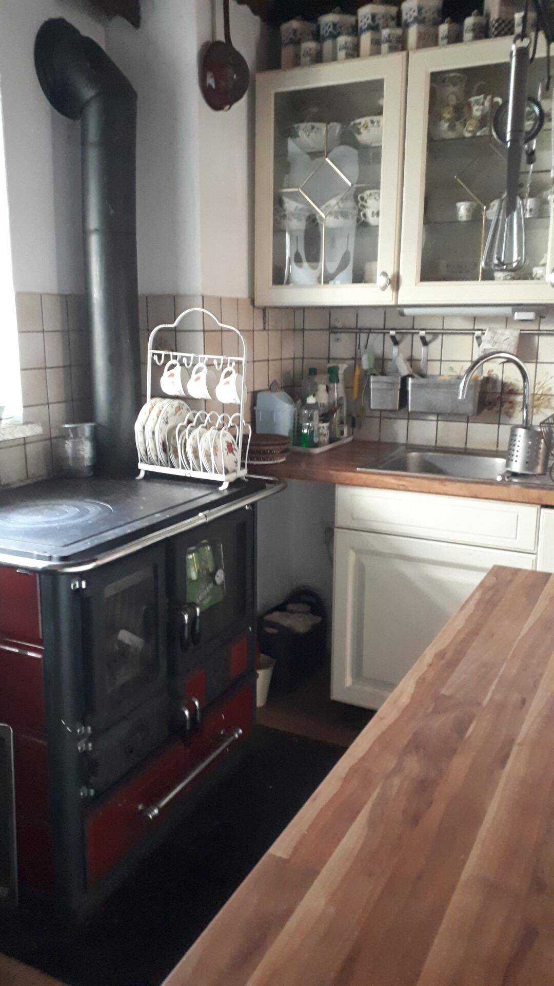 Rustikale Küche mit Holzofen, Arbeitsplatte aus Holz und traditionellen Hängeschränken.