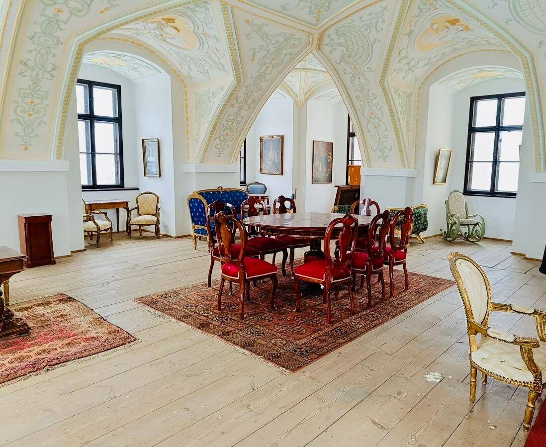 Großer Speisesaal mit gewölbter Decke, Holzboden und mehreren antiken Esstischen mit roten Stühlen.