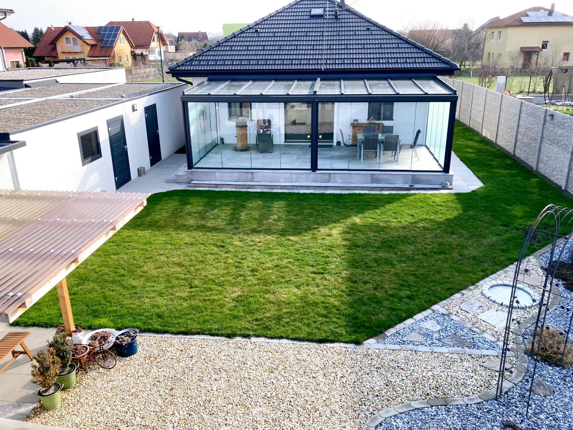 Blick auf das moderne Haus mit großem Wintergarten, gepflegtem Rasen und Kiesweg im Garten.