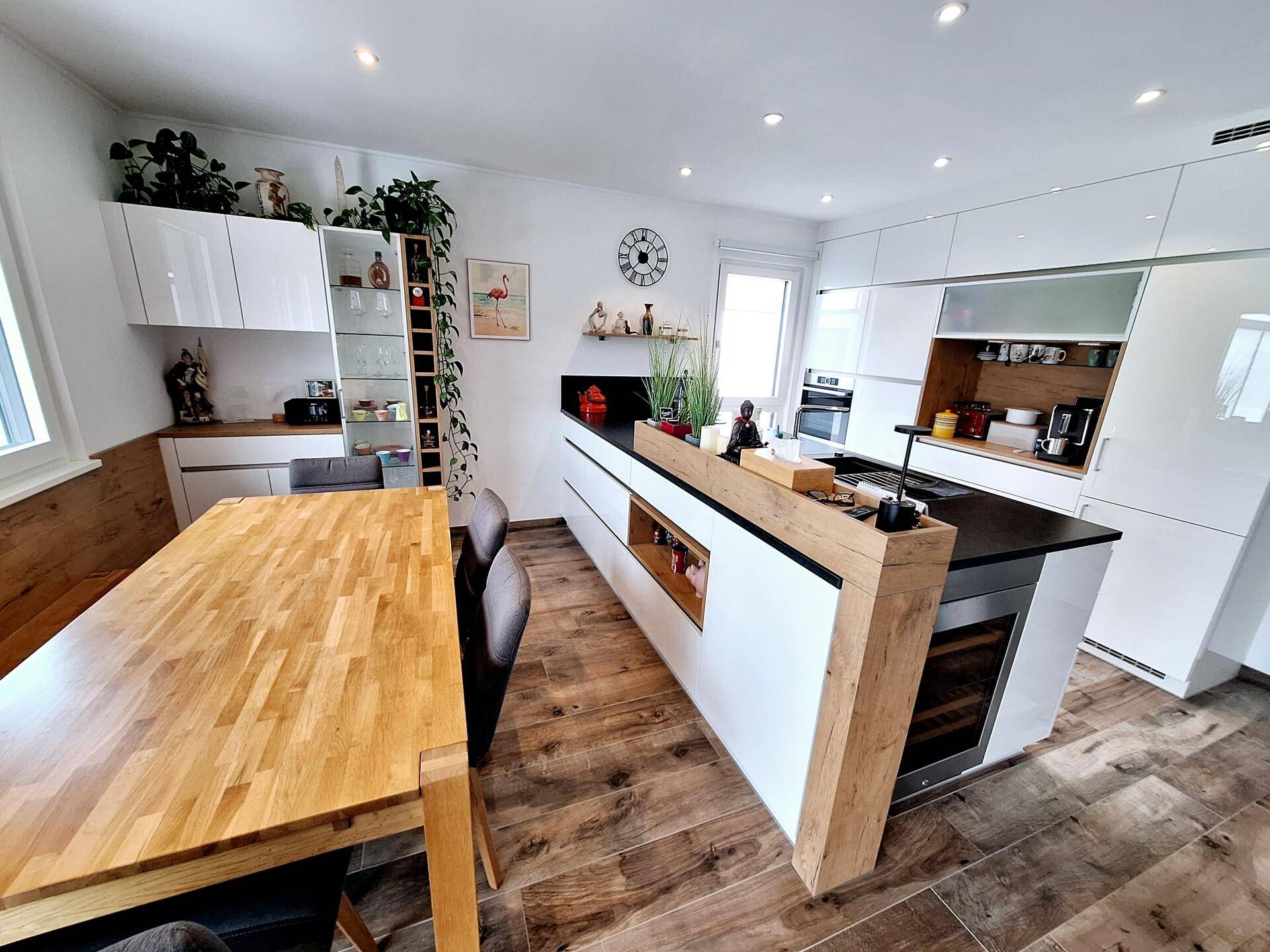 Helle, moderne Küche mit weißen Schränken, Kochinsel und Essbereich mit Holztisch und Bank.
