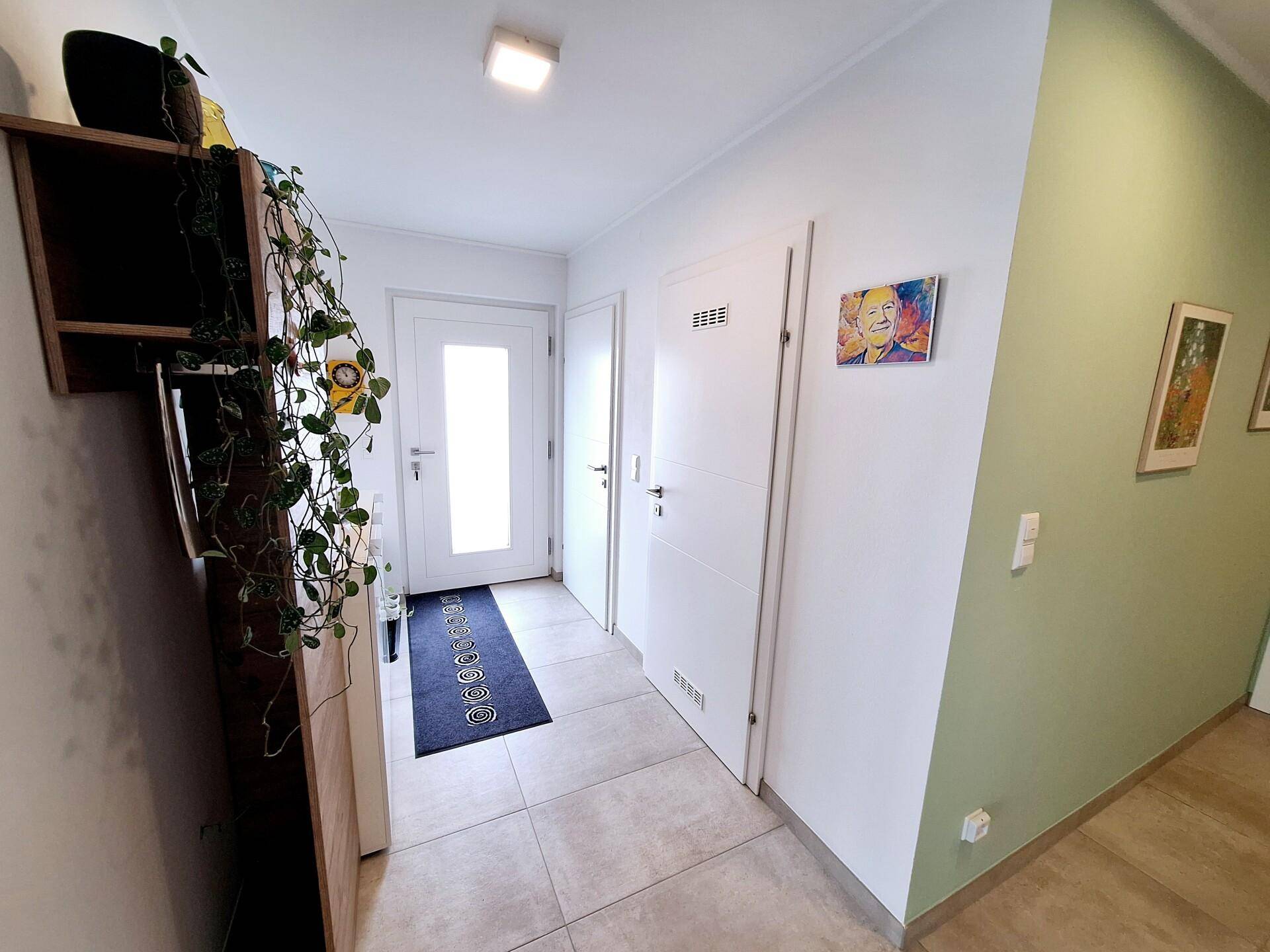 Heller Eingangsbereich mit Fliesenboden, weißer Tür und einer Garderobe mit Pflanzen.