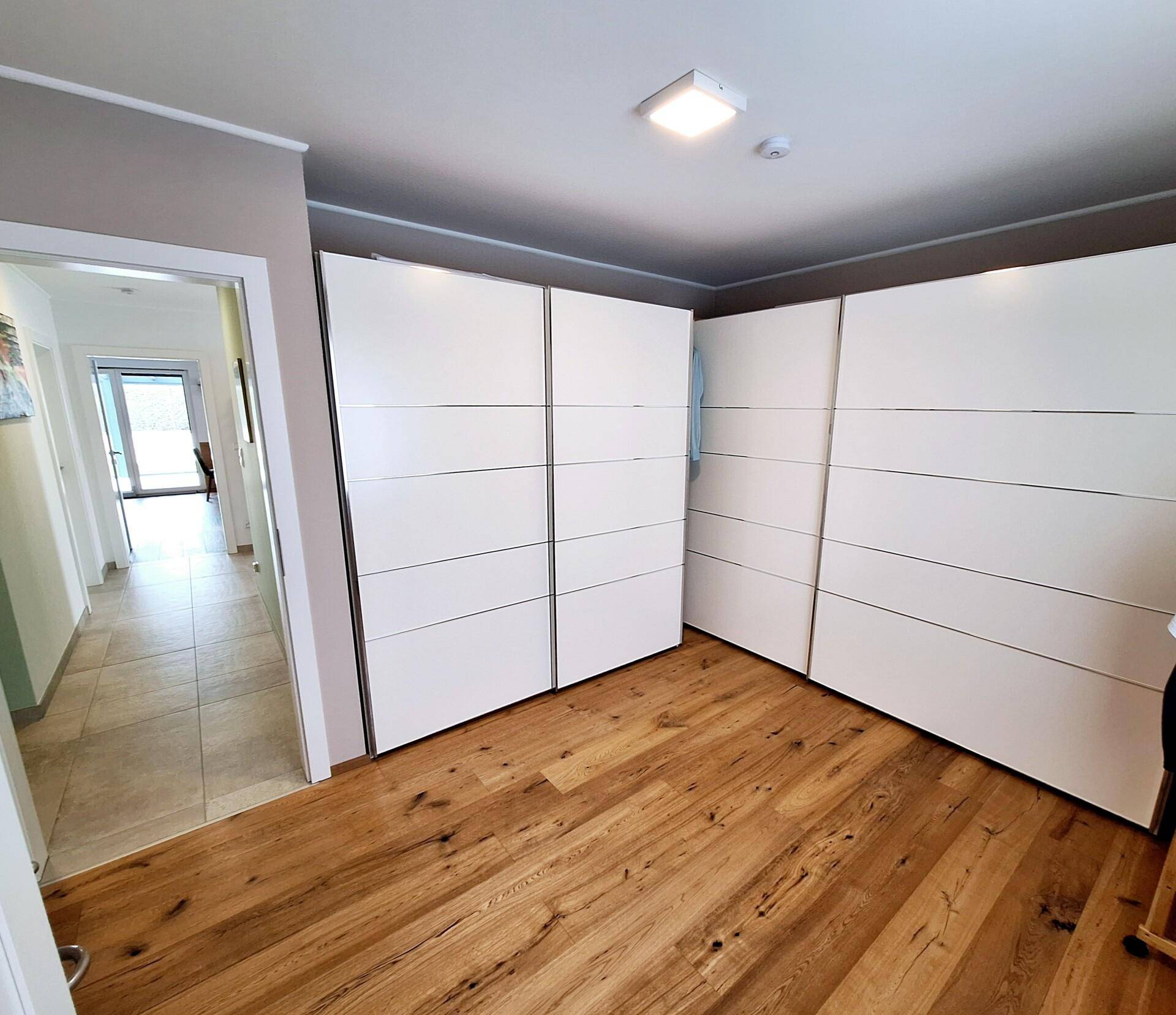 Schlafzimmer mit hellem Holzboden und großen, modernen Einbauschränken für viel Stauraum.