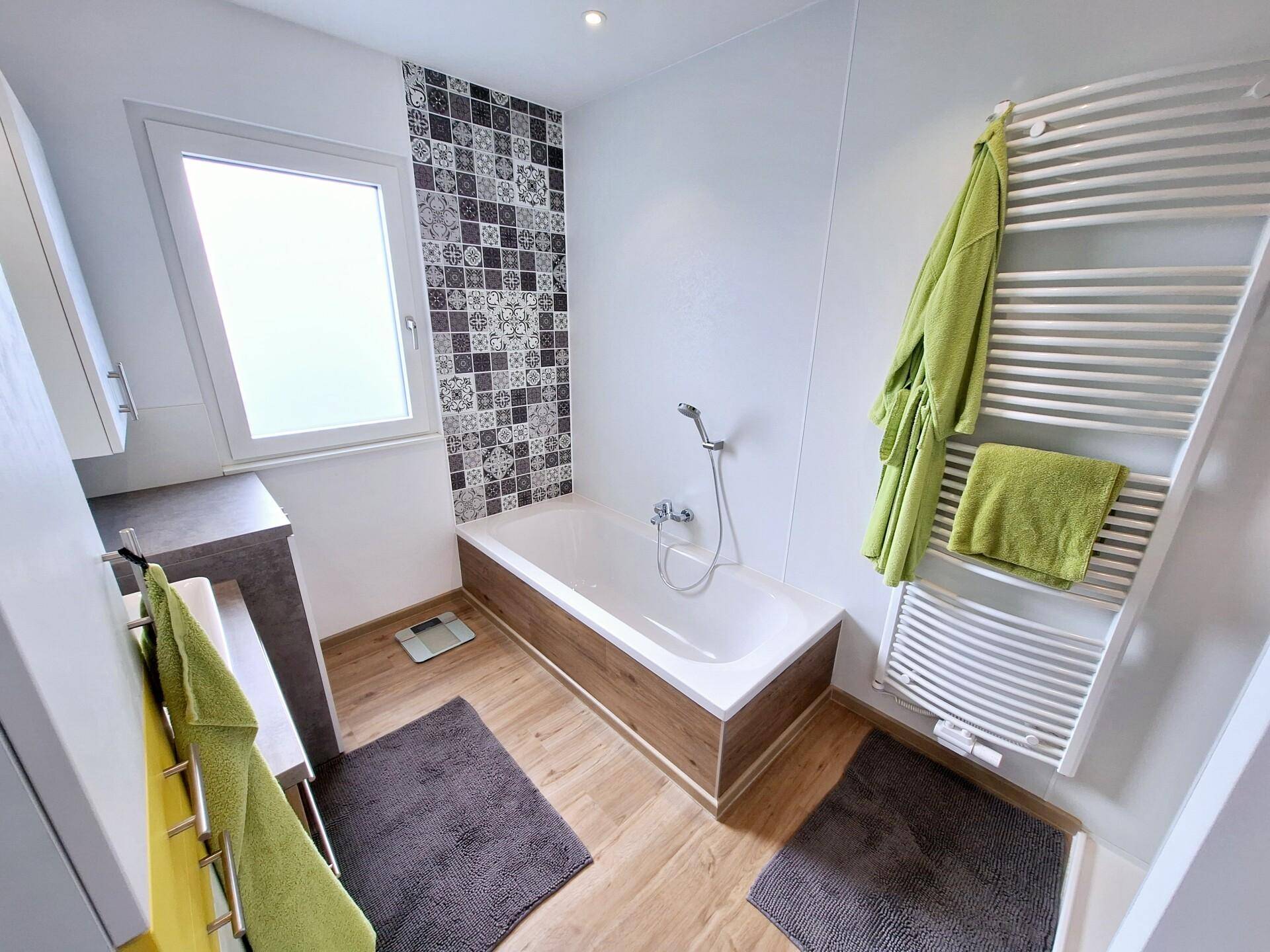 Modernes Badezimmer mit Badewanne, gemusterten Fliesen und beheiztem Handtuchhalter.
