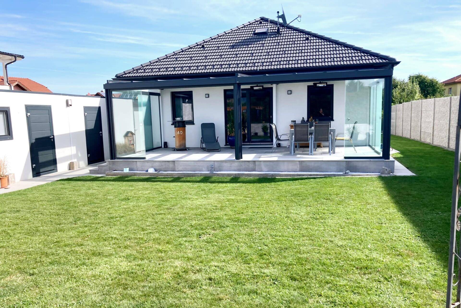 Das moderne Einfamilienhaus mit großem Wintergarten und gepflegtem Rasen unter blauem Himmel.