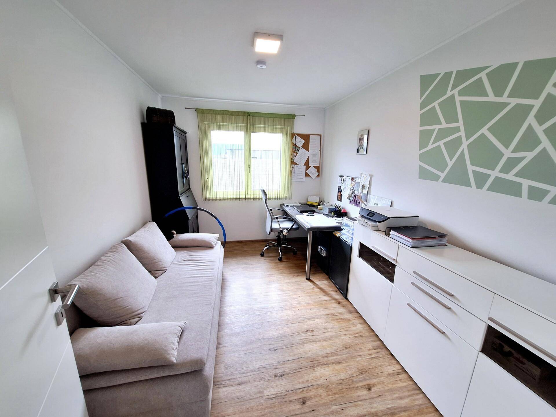 Helles Arbeitszimmer mit Schreibtisch, Sofa und praktischen weißen Schränken.