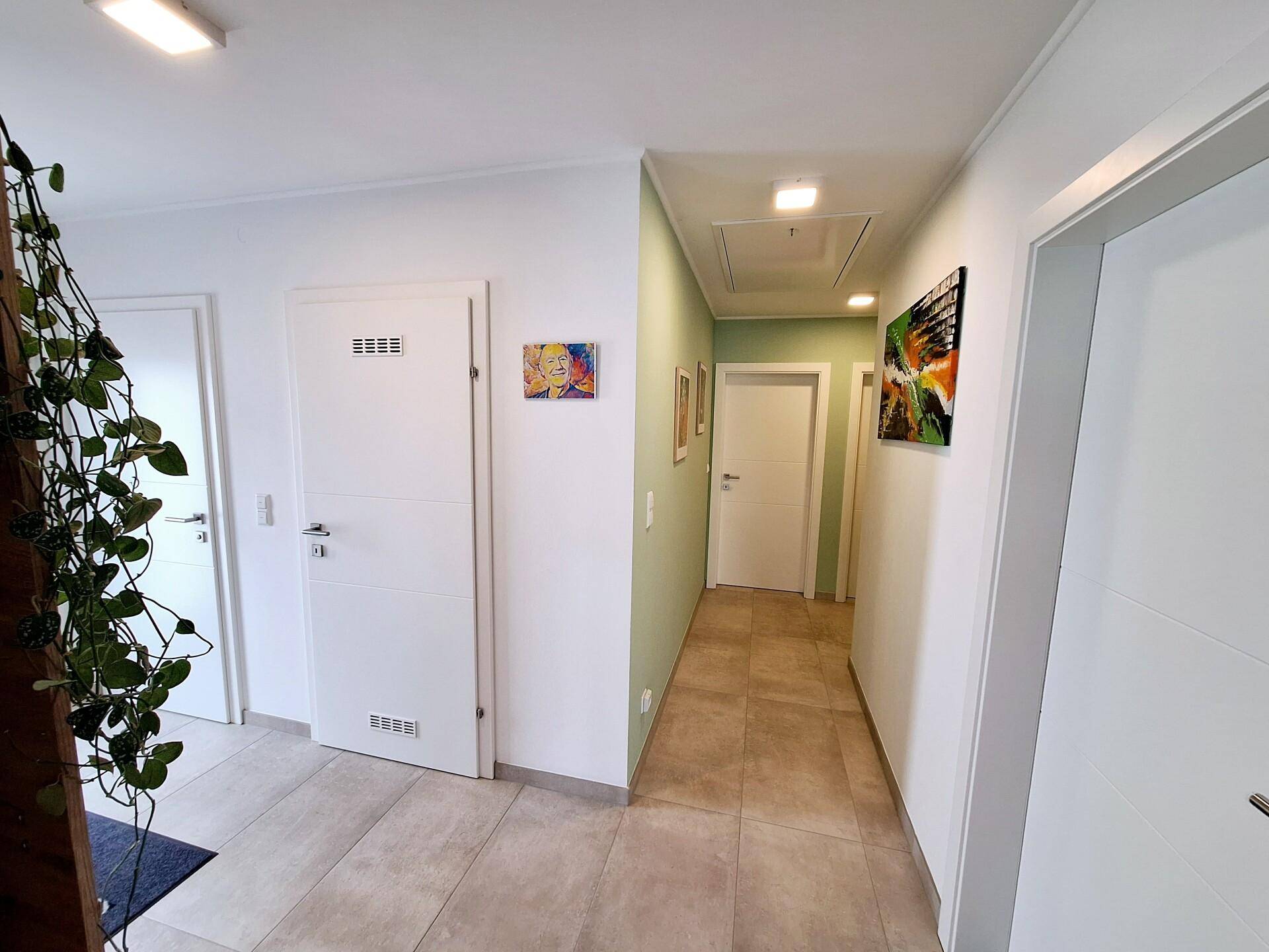 Heller Eingangsbereich mit Fliesenboden, weißer Tür und moderner Kunst an der Wand.