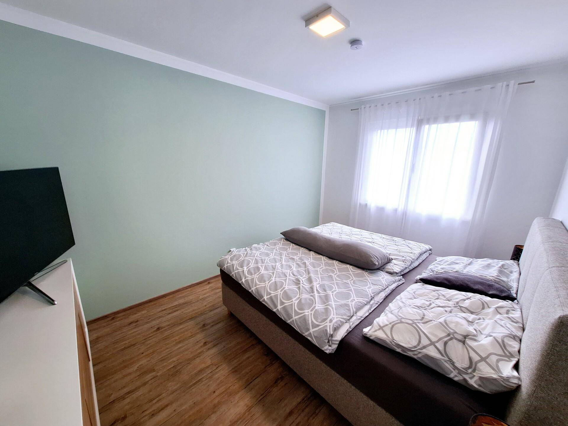 Helles Schlafzimmer mit Doppelbett, Holzboden und einer dezent grünen Akzentwand.