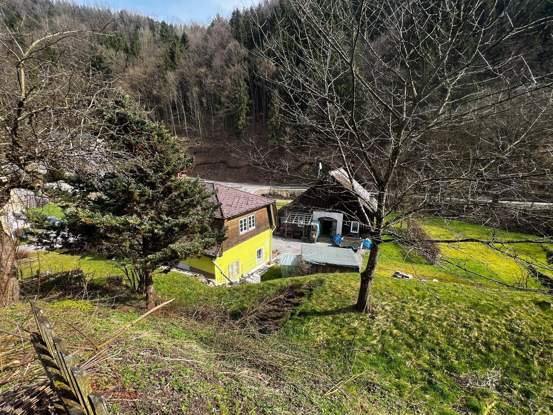 Erhöhte Ansicht des gelben Hauses und der Scheune, umgeben von grünen Hügeln und Bäumen.