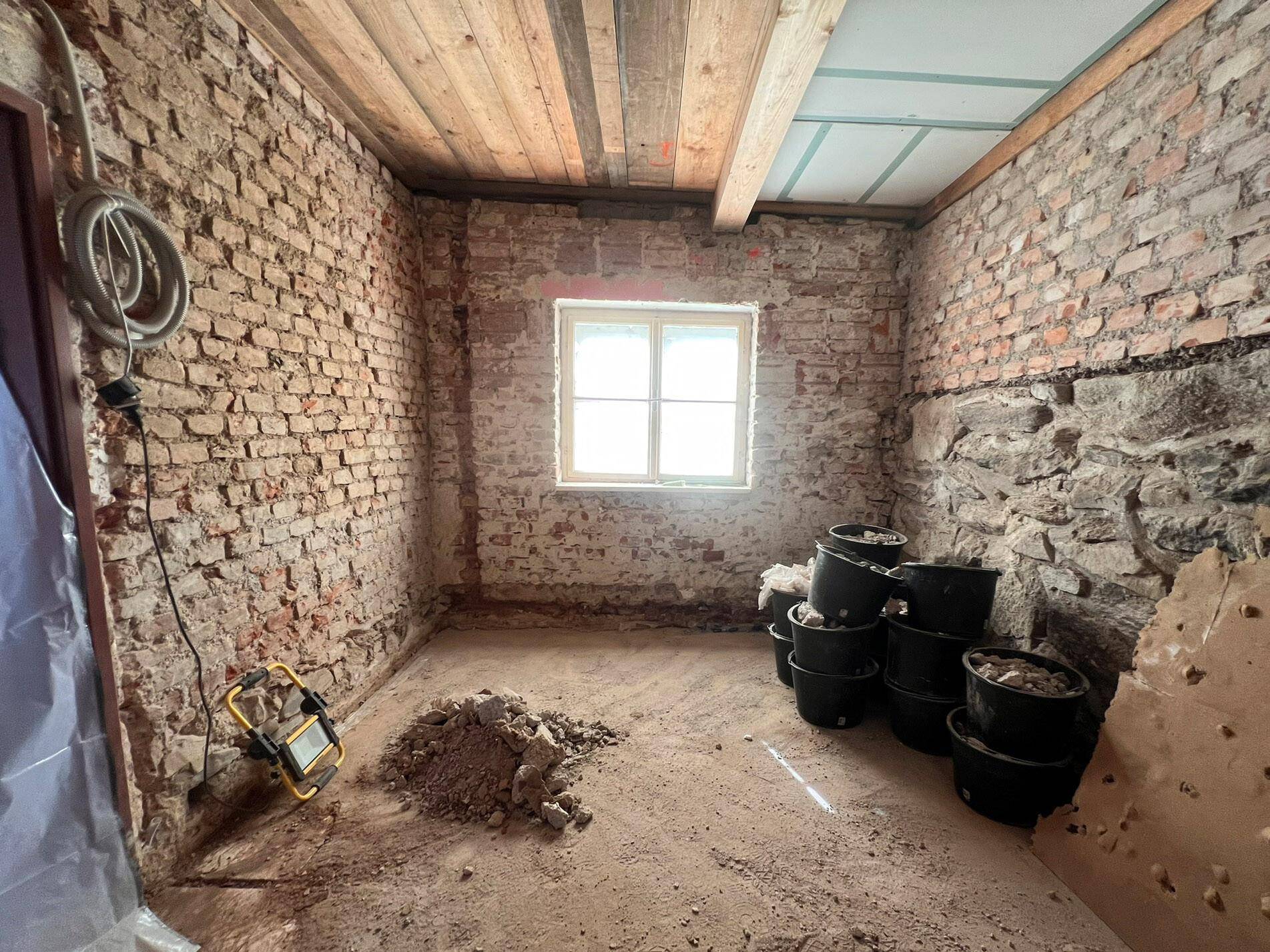 Renovierungsbedürftiger Raum mit freigelegten Ziegel- und Steinwänden sowie Holzbalkendecke.