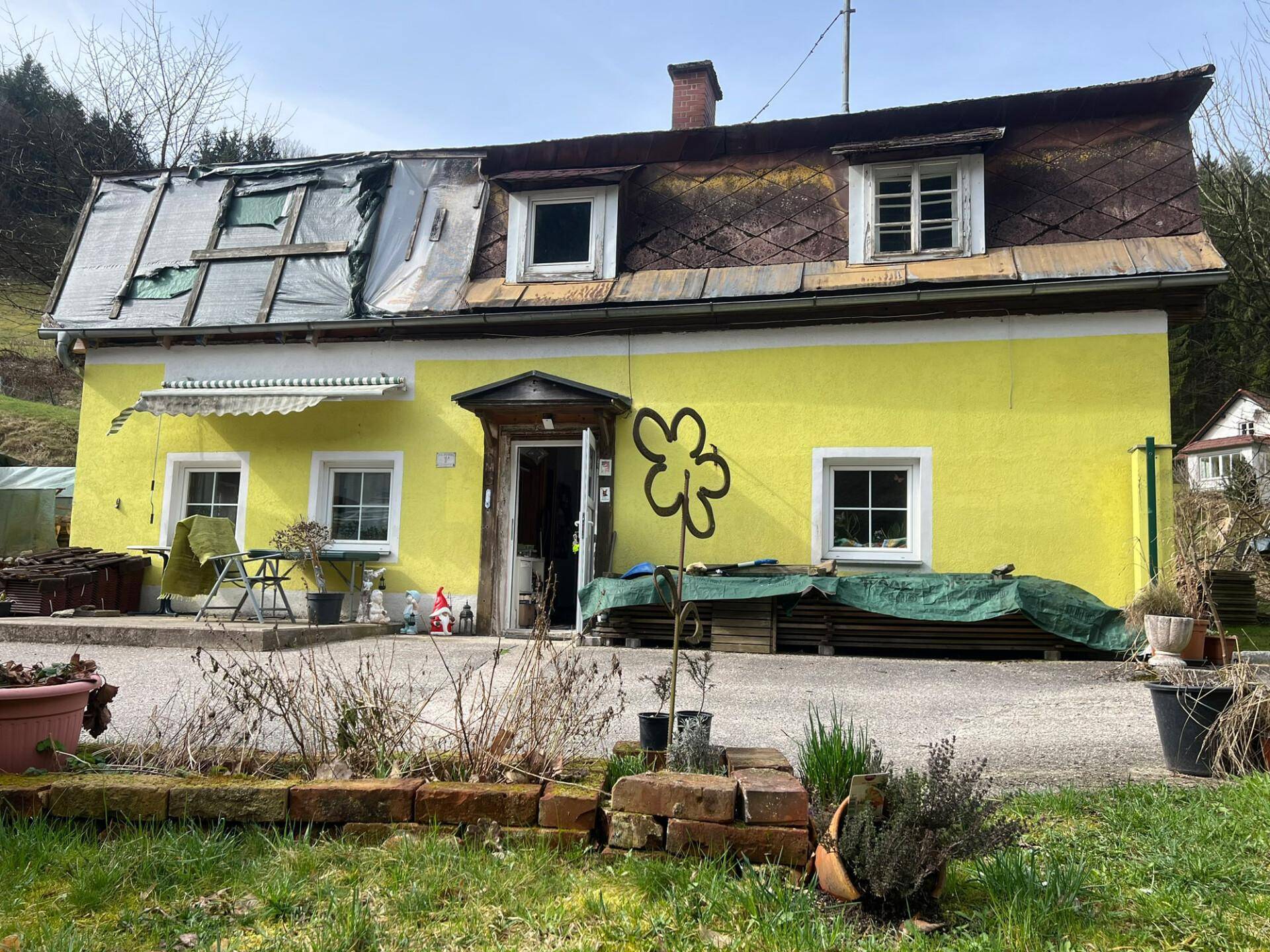 Vorderansicht des gelben Hauses mit teilweise abgedecktem Dach, das seinen rustikalen Charme zeigt.
