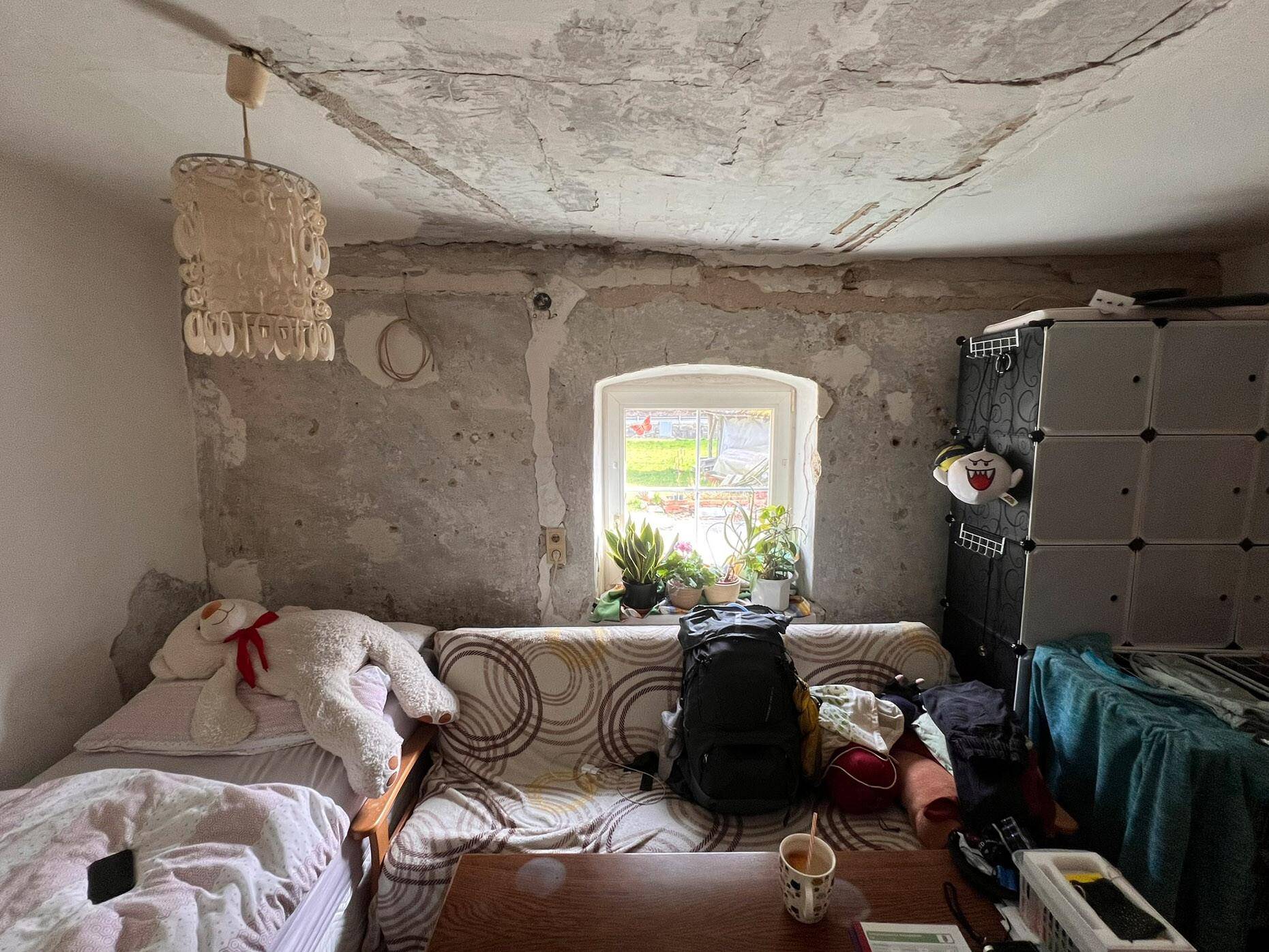 Wohn- oder Schlafzimmer mit Schlafsofa, rauen Wänden und einem Fenster mit Blick ins Grüne.