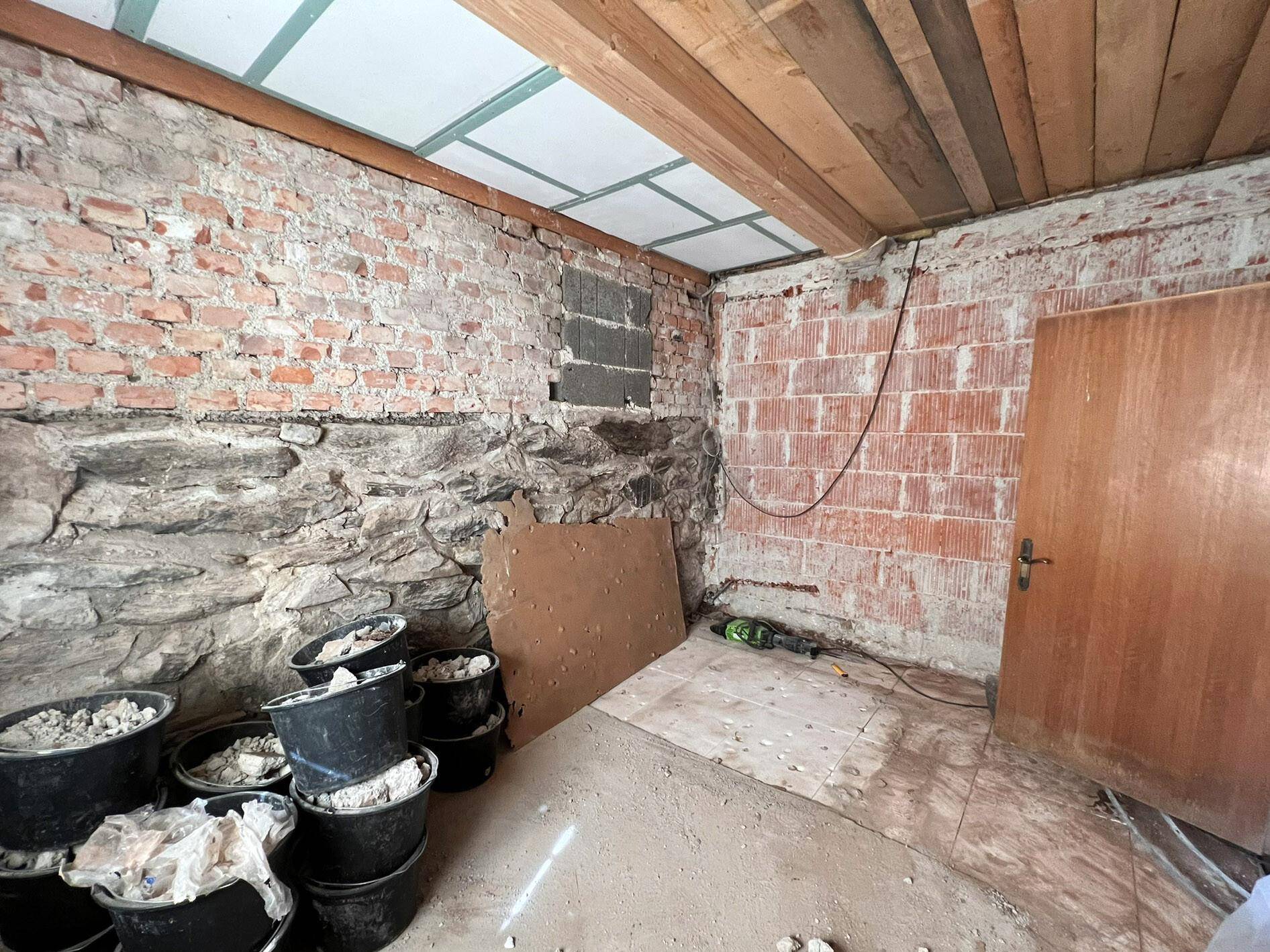 Renovierungsbedürftiger Raum mit freigelegten Ziegel- und Steinwänden sowie Holzbalkendecke.